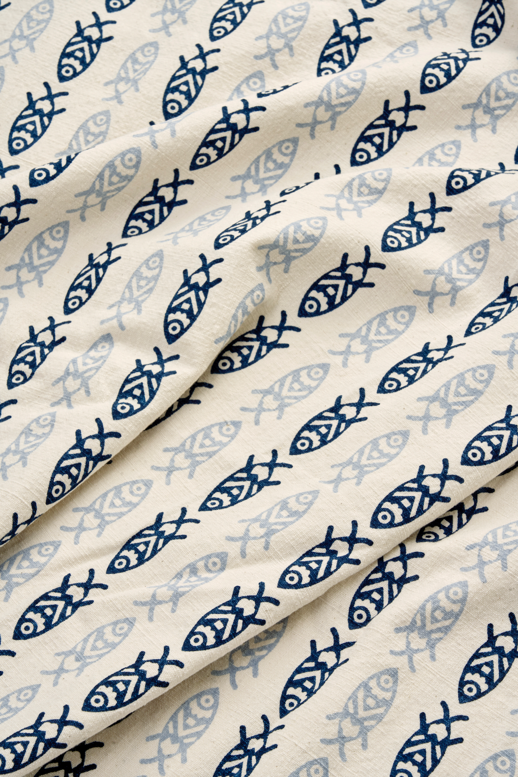 Close up of navy blue fish pattern on a cream colored cotton tablecloth fabric with soft folds.