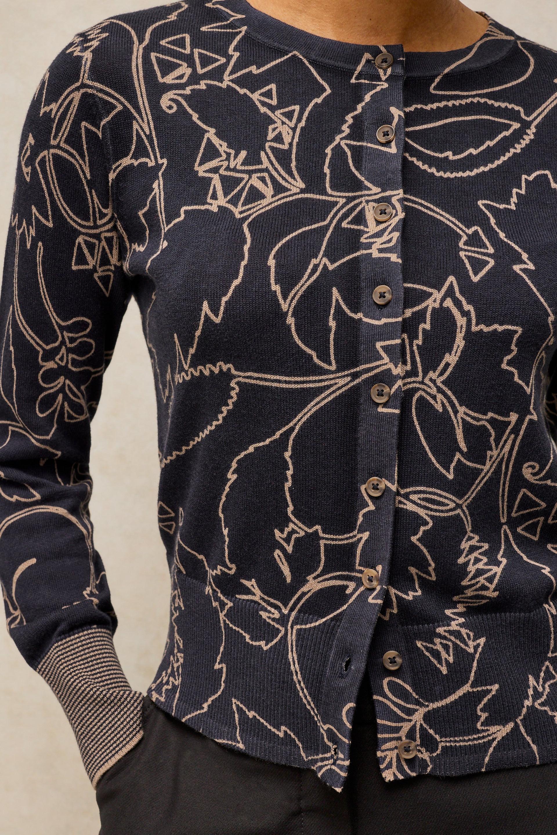 A close-up of a navy blue cardigan sweater with a beige line-art botanical pattern, featuring a button-up front and ribbed cuffs.