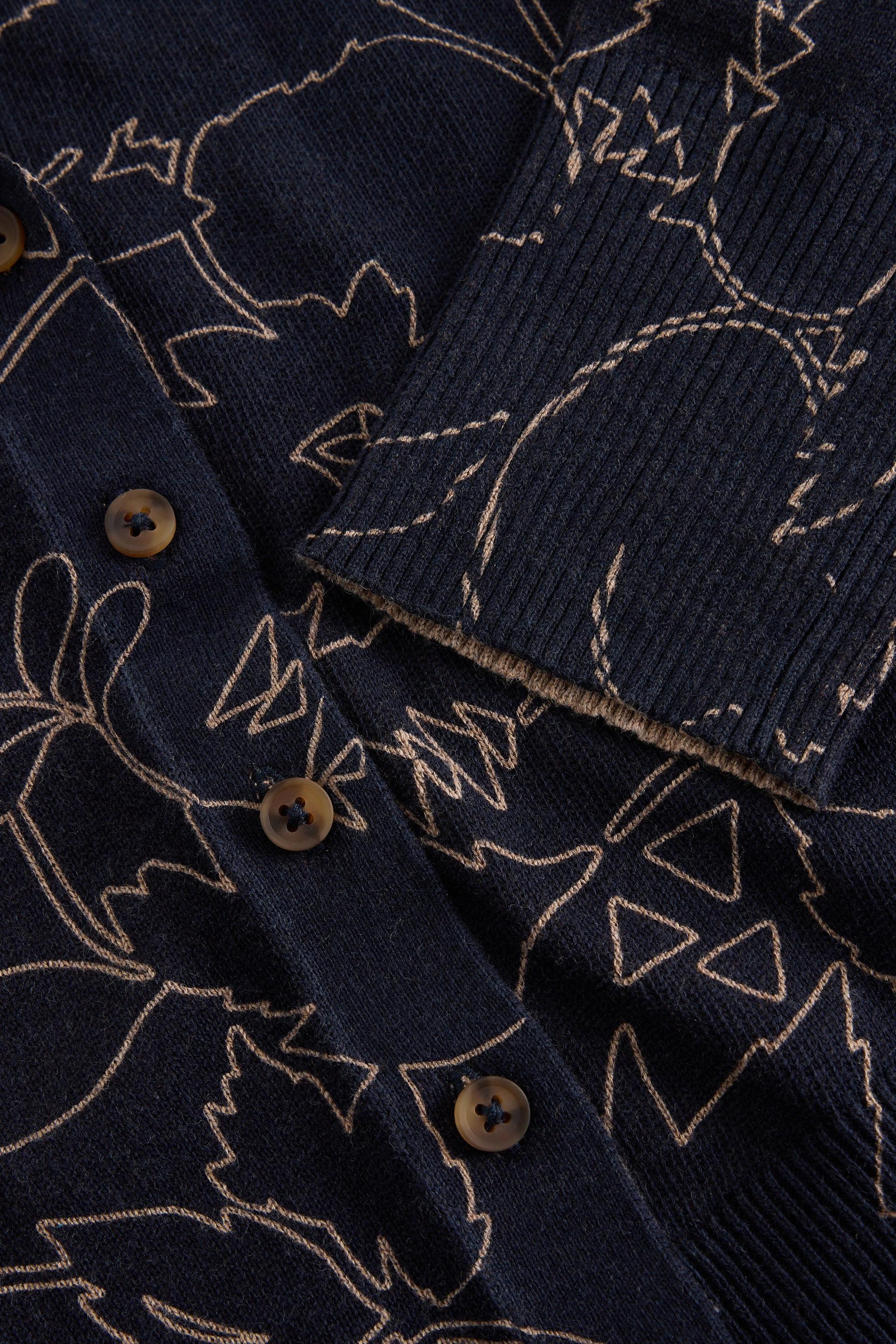Close-up of a dark navy ribbed knit garment with a beige embroidered abstract line pattern and brown buttons.