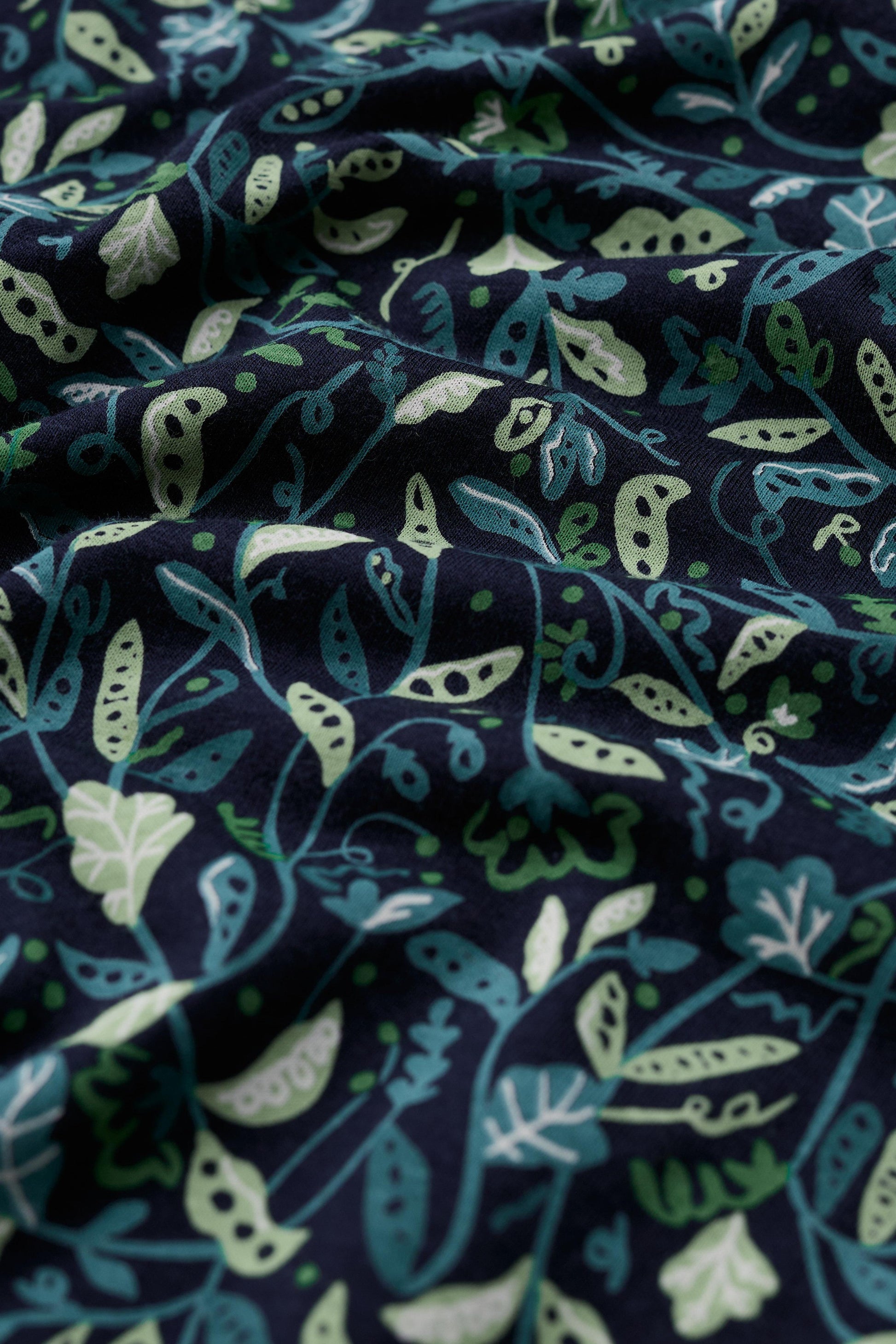 Close up of navy blue organic cotton fabric with a light and dark green botanical leaf and pod print pattern.