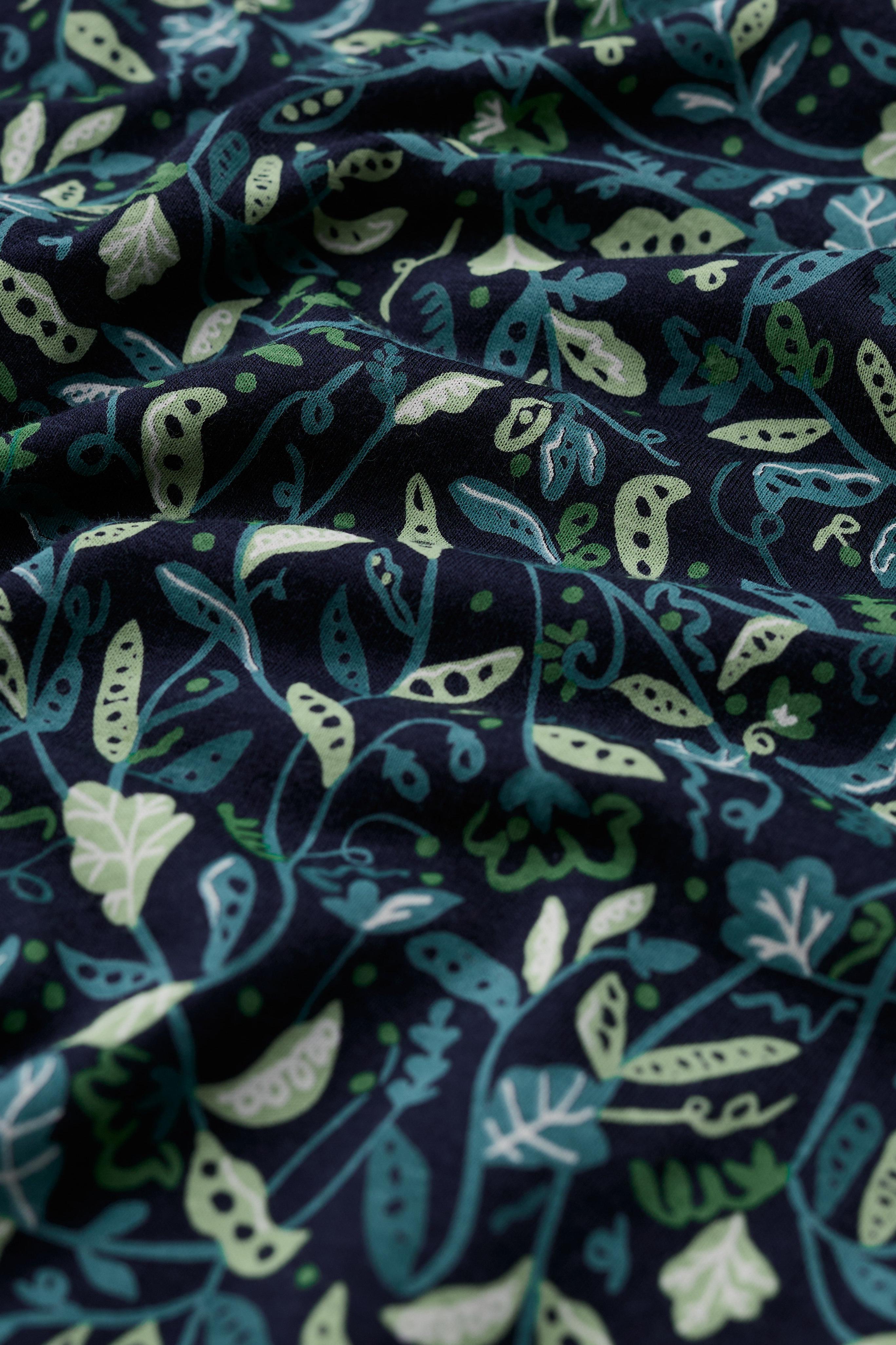 Close up of navy blue organic cotton fabric with a light and dark green botanical leaf and pod print pattern.