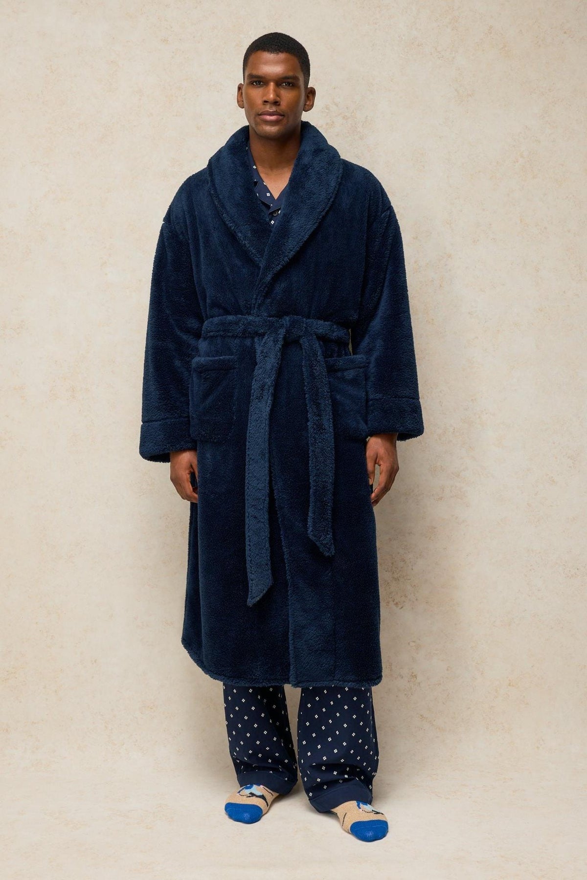 Man wearing a navy fluffy men's dressing gown over printed pyjamas.