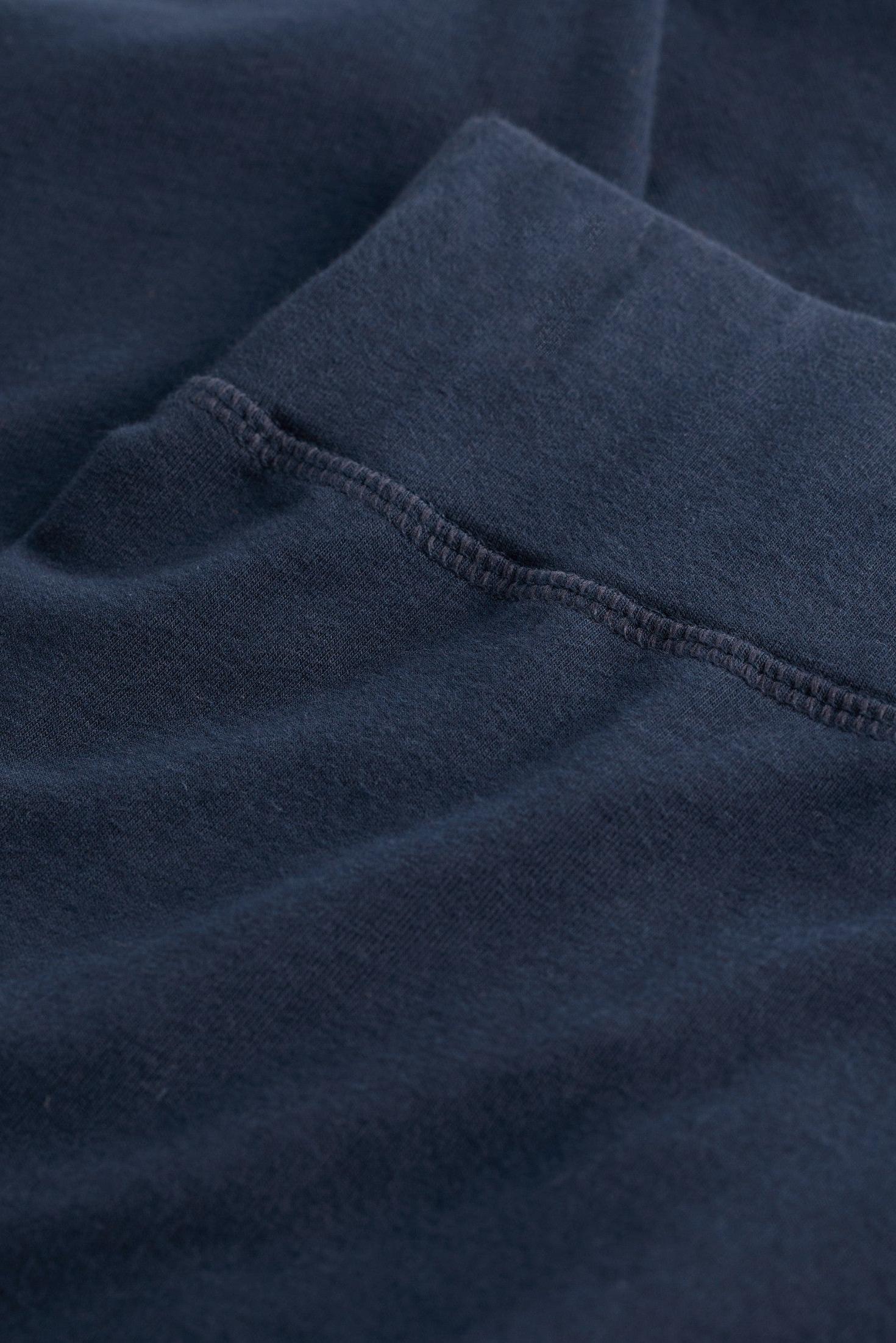 Close-up of a dark navy blue fabric garment, showing the texture of the material and a neat hemstitch detail.
