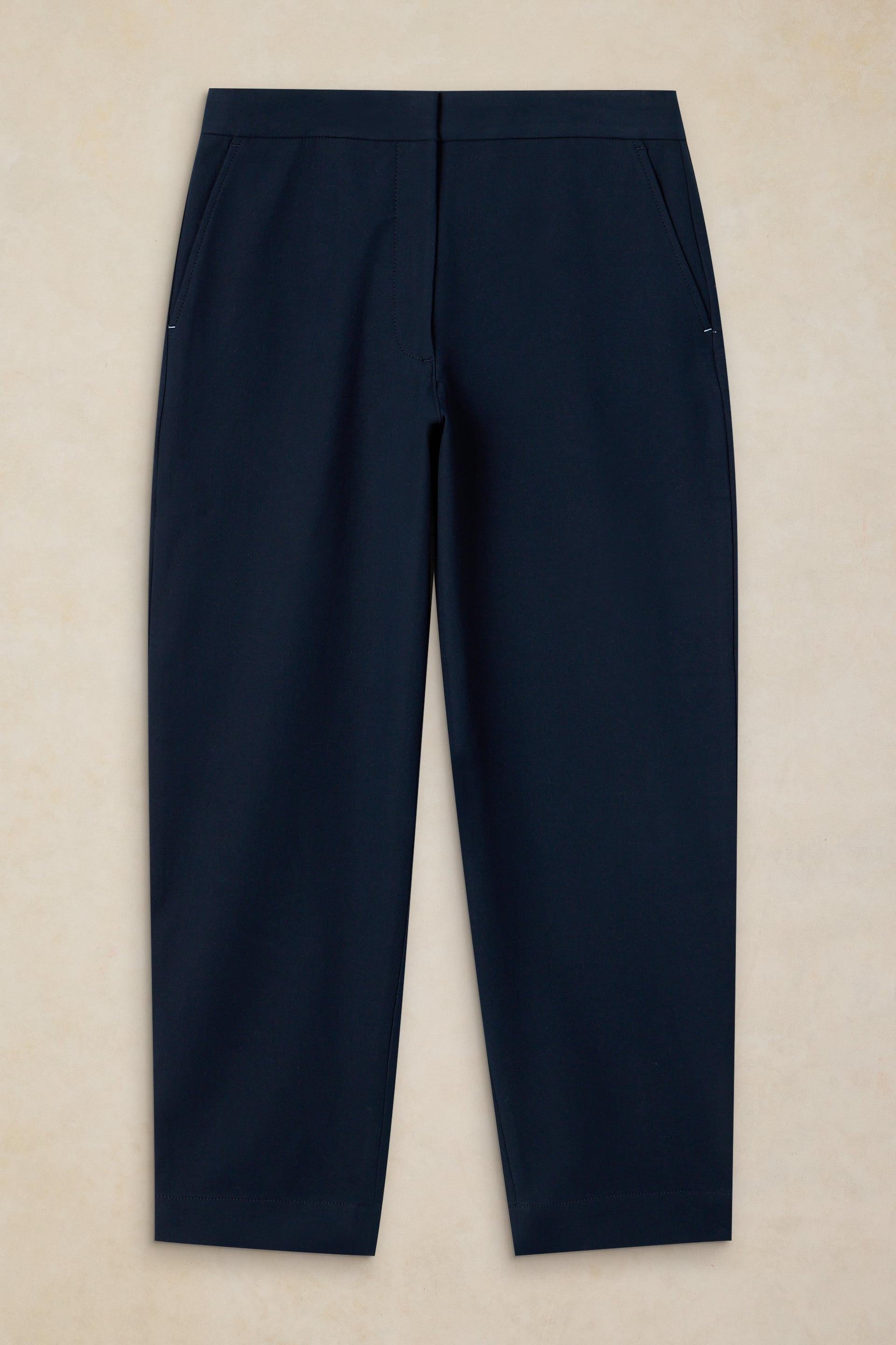 A pair of dark navy blue trousers laid flat against a light beige textured background.