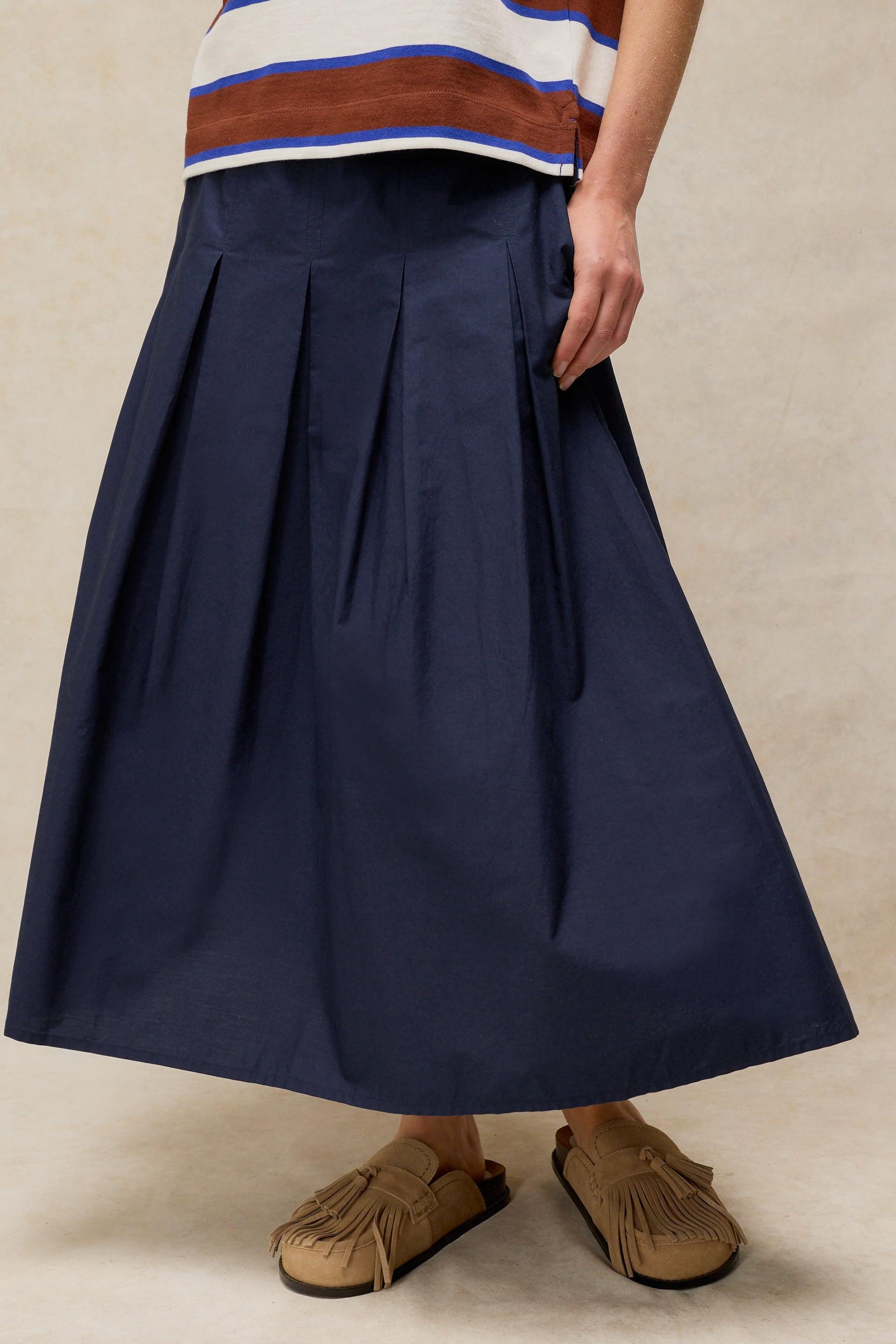 A person wearing a navy blue pleated midi skirt made of organic cotton with beige tassel loafers