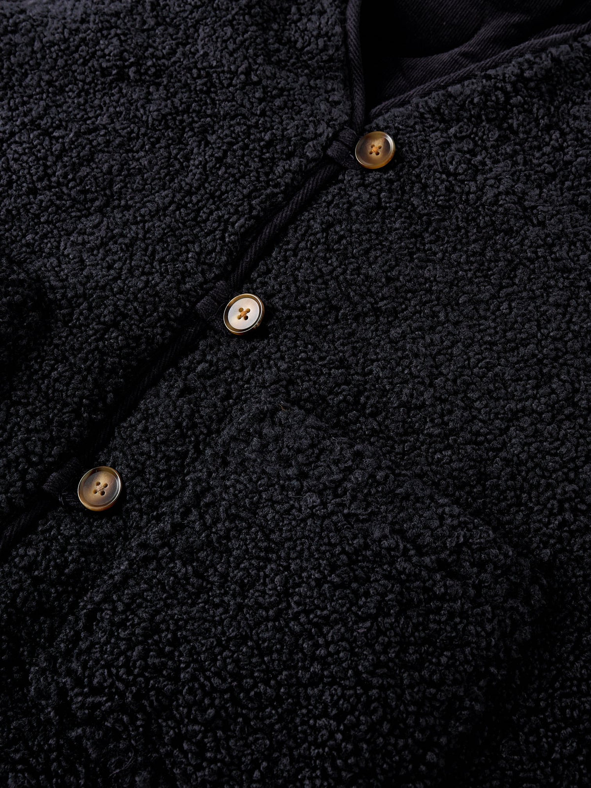 Close up detail of a navy blue textured reversible gilet with brown buttons, made from recycled polyester.