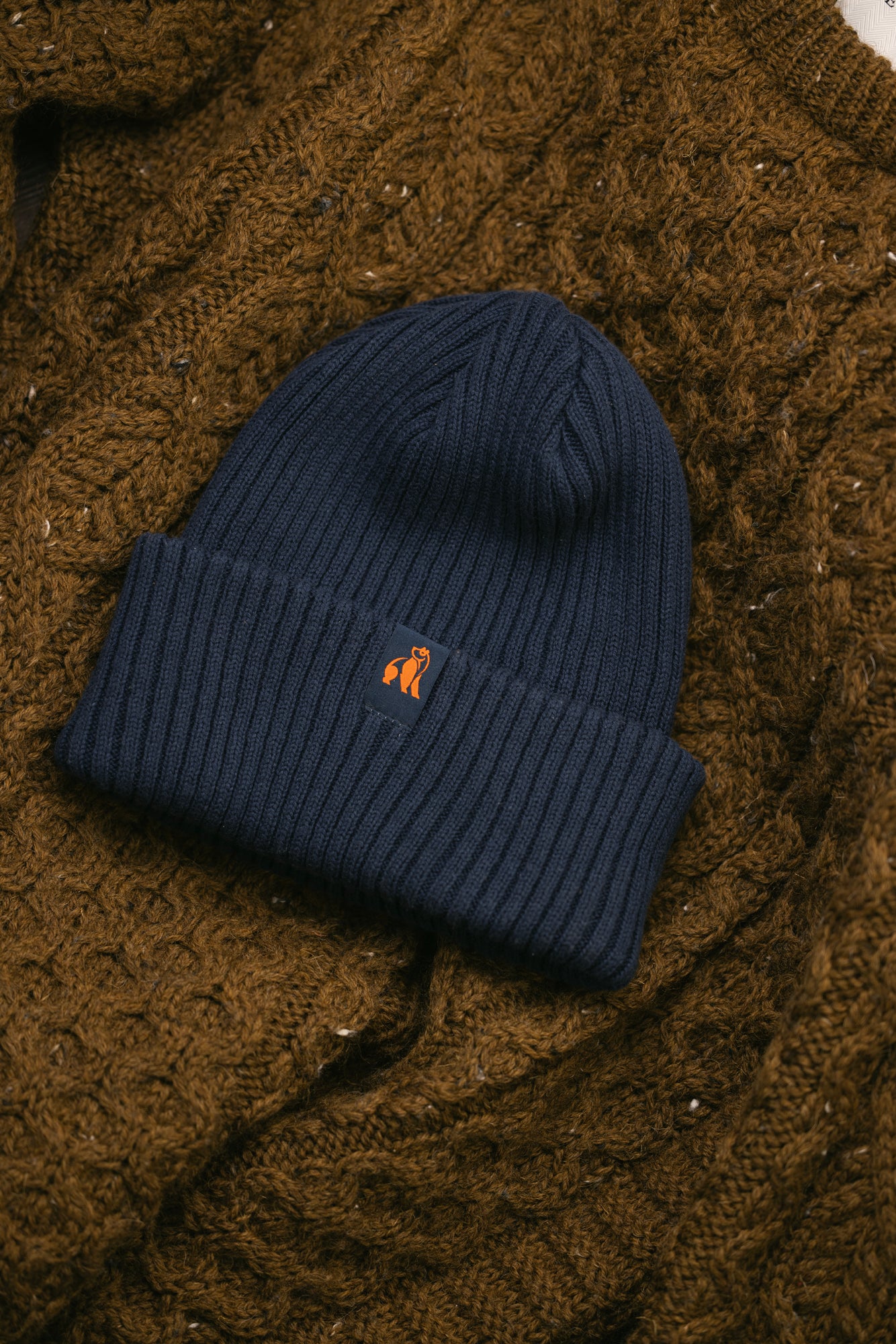 A navy ribbed Swole Panda beanie made from organic cotton sitting on top of a brown cable knit sweater.