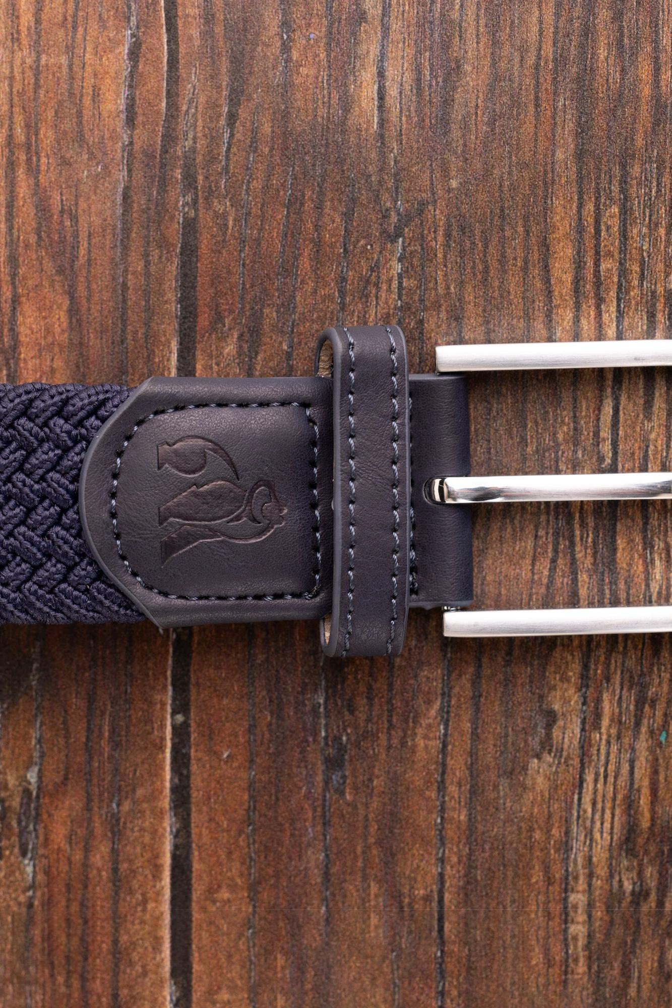 Close-up of a navy woven belt featuring a silver buckle and embossed leather tab on a wooden background.