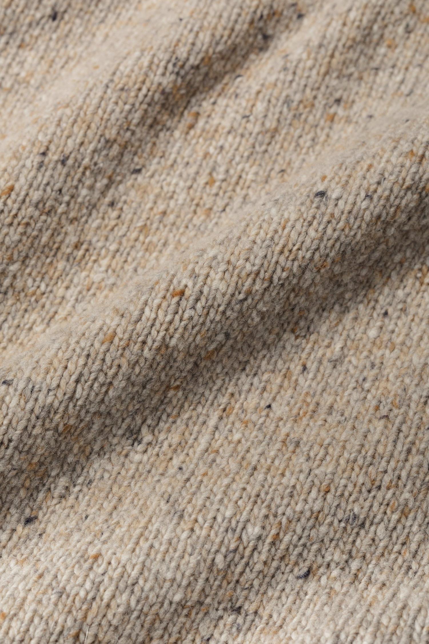 Close-up texture of a soft, neutral colour wool jumper with flecked details.