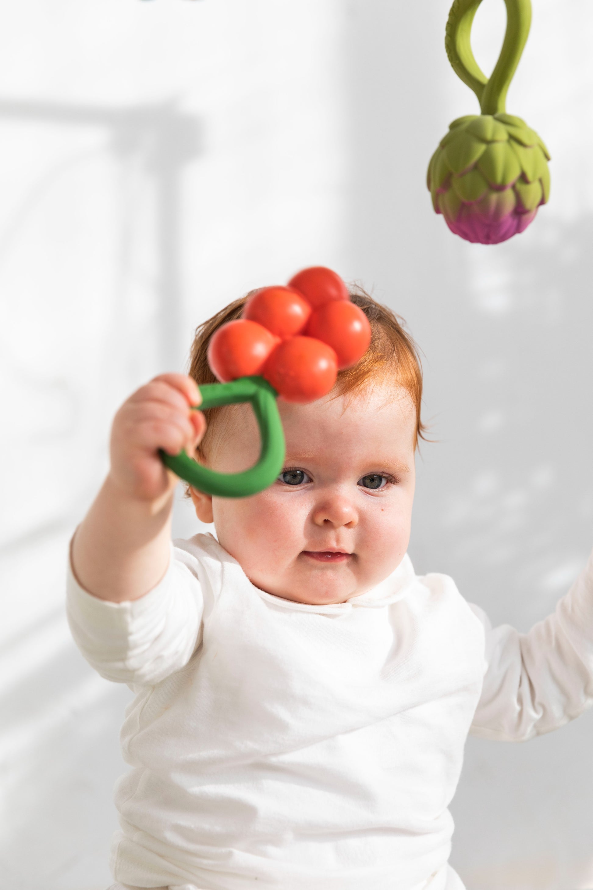 Baby holding a 2-in-1 teether and calming rattle from Oli&Carol.