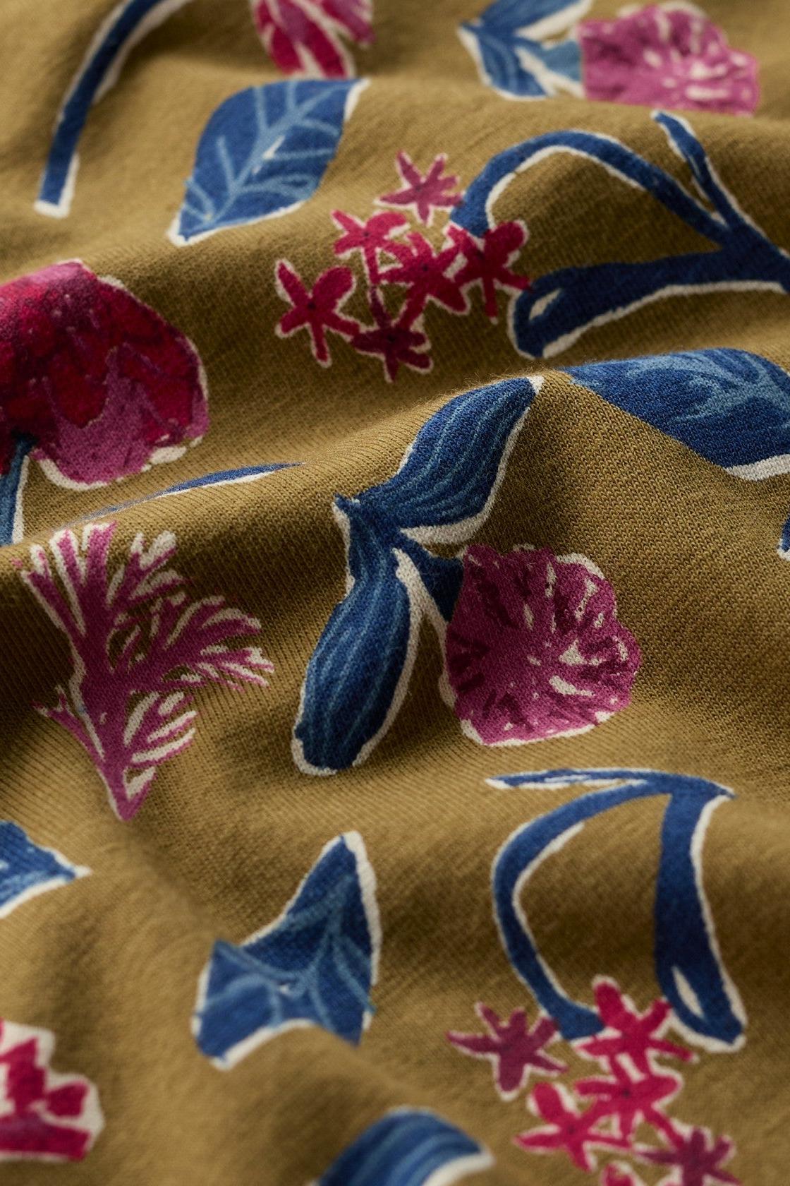 Close-up of olive green organic cotton fabric featuring a vibrant floral and leaf print pattern