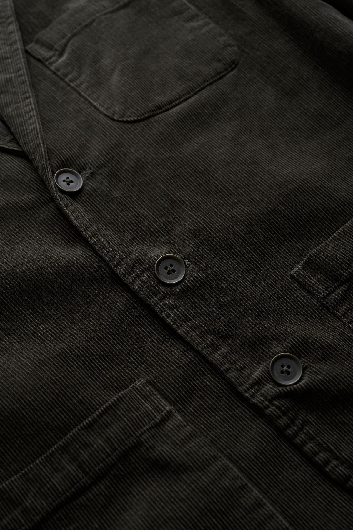 Close up of an olive green men's corduroy blazer with three buttons and front pockets.