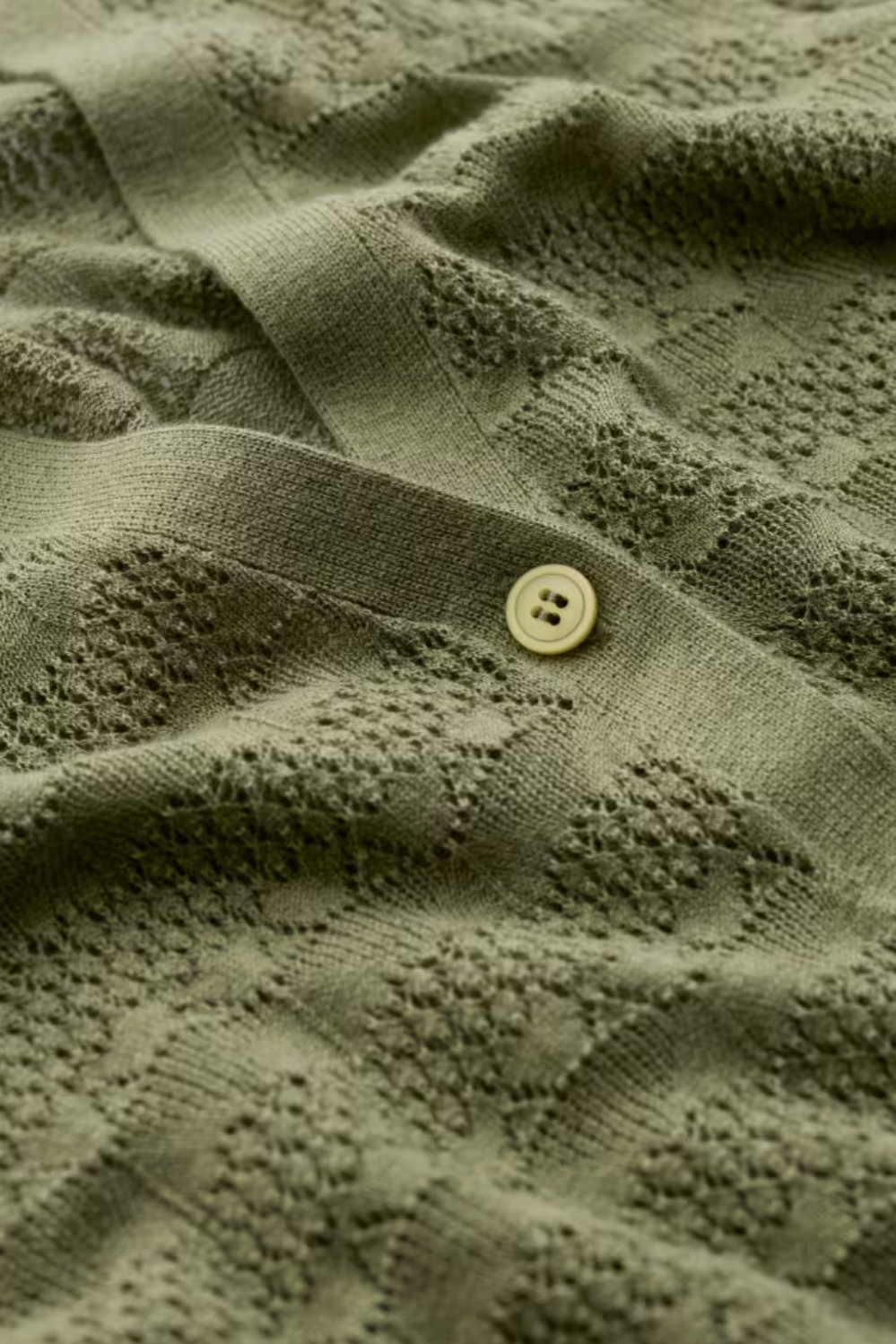Close-up of a textured olive green organic cotton cardigan with a button detail.