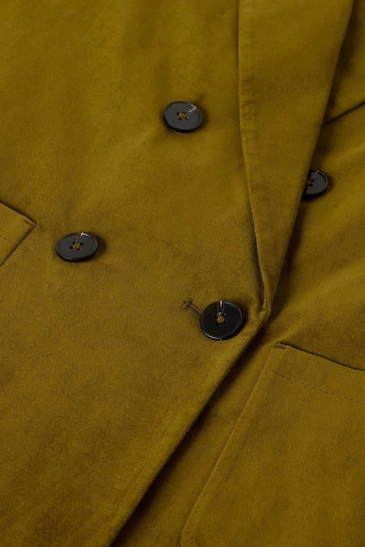 Close up detail of an olive green velvet blazer with dark buttons suitable for office or evening wear.
