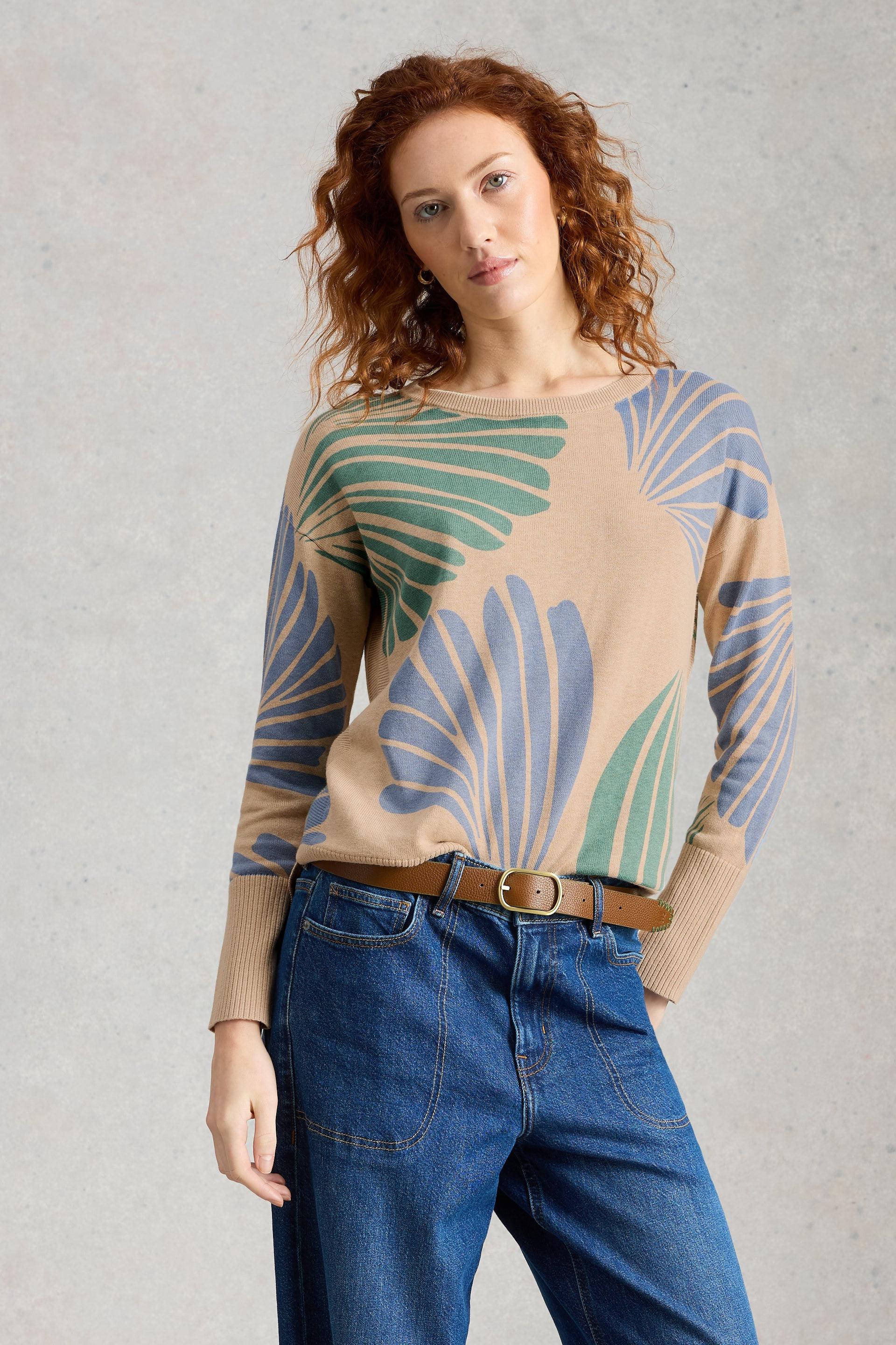 Woman wearing a patterned organic cotton sweater and blue jeans against a gray background