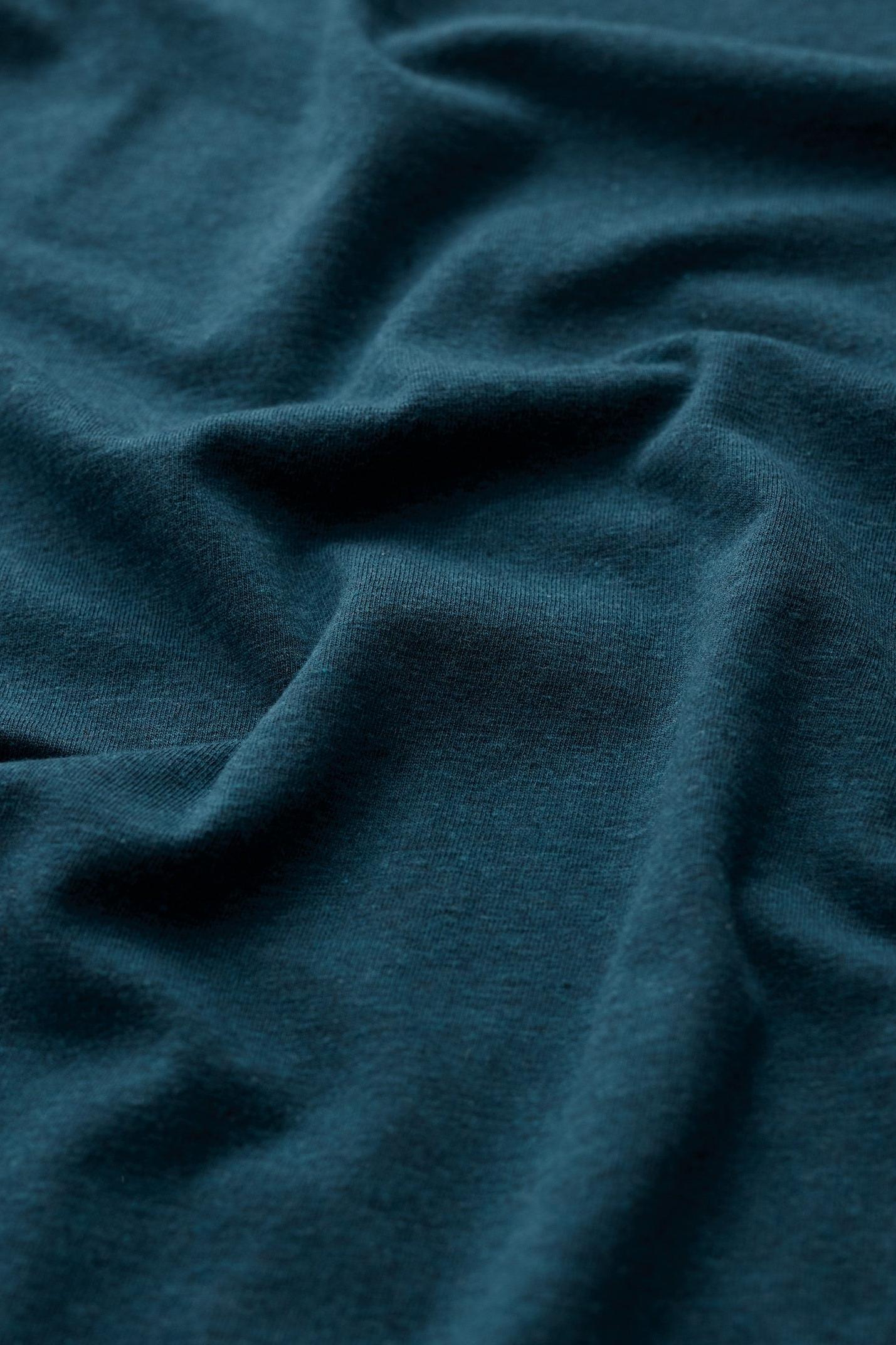 Close-up of soft organic cotton fabric in a deep teal blue colour with gentle folds.