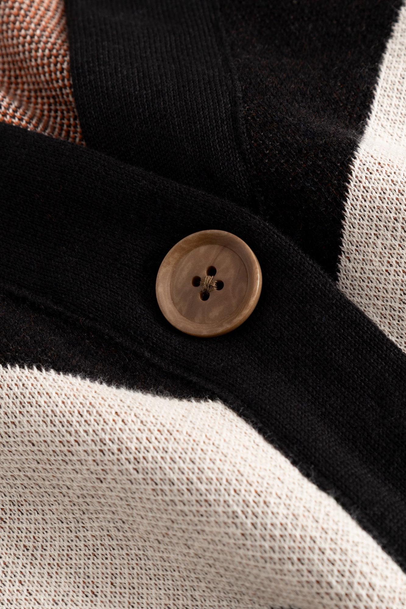 Close-up of a knit cardigan with black, cream, and tan color-blocked panels, featuring a single round brown button.