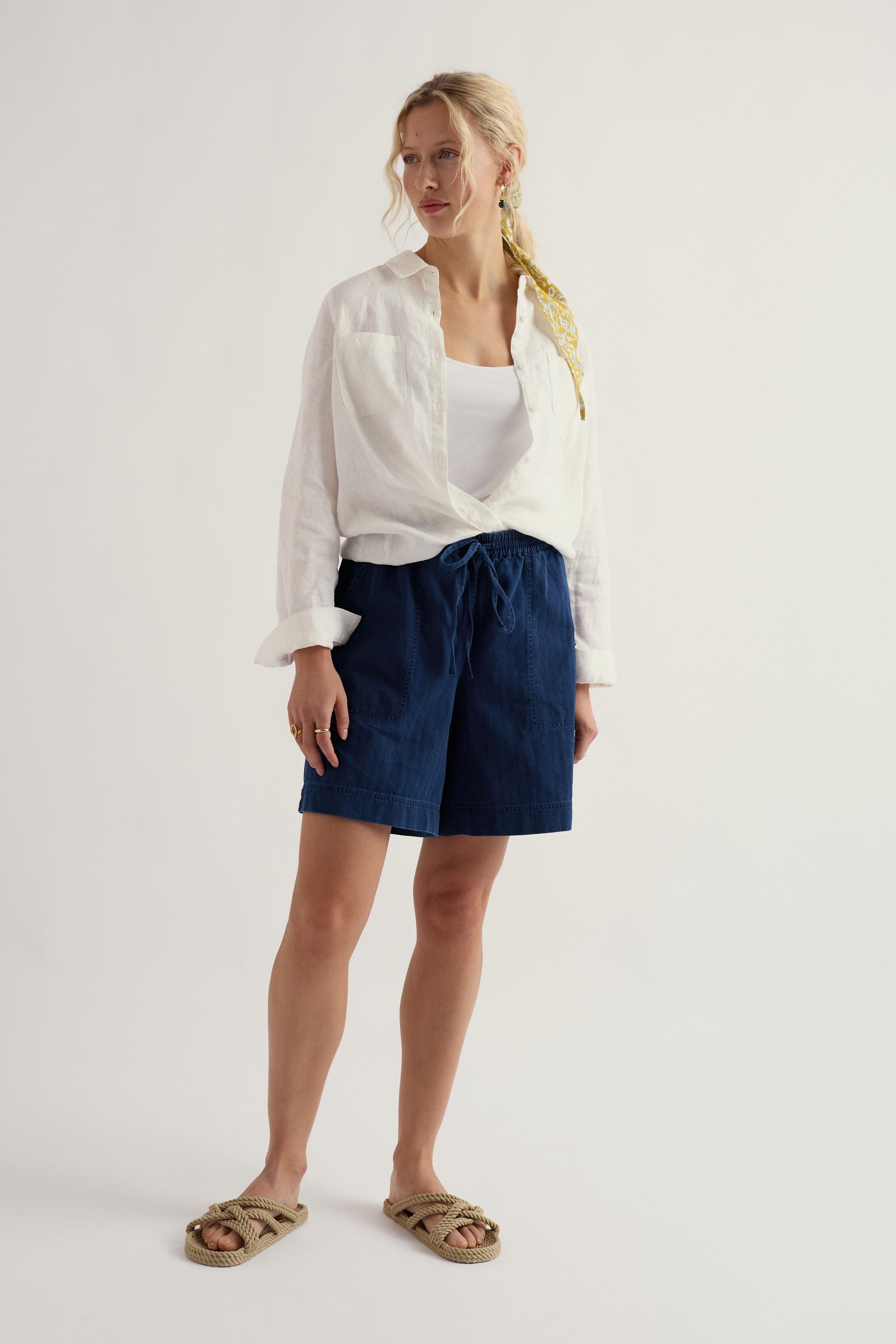 Woman wearing a white shirt and blue shorts on a plain background