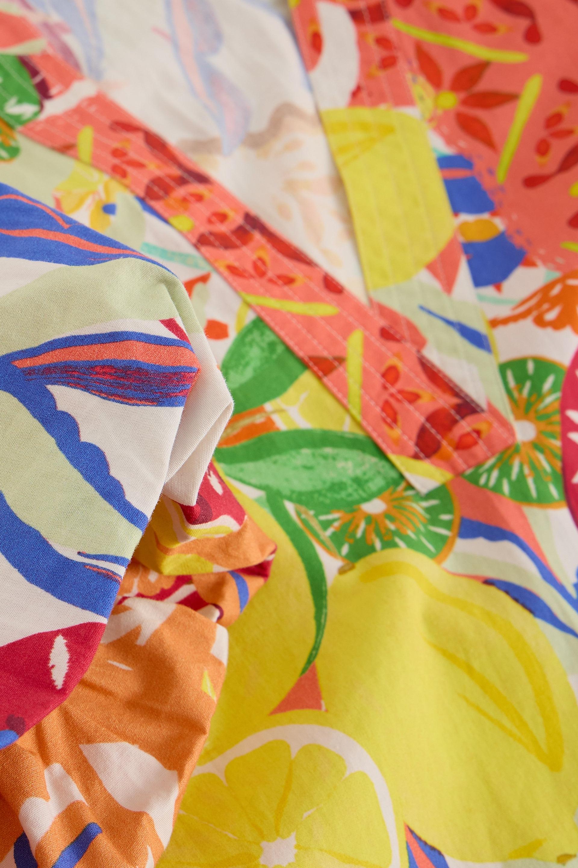 Close-up of vibrant organic cotton fabric featuring a colourful citrus fruit and tropical leaf print pattern.