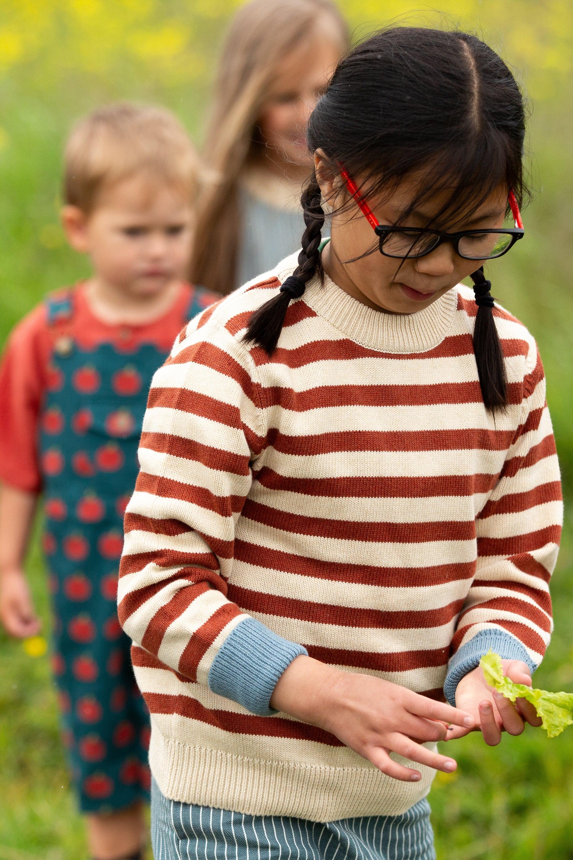 Child wearing a striped organic cotton knit sweater in a grassy outdoor setting