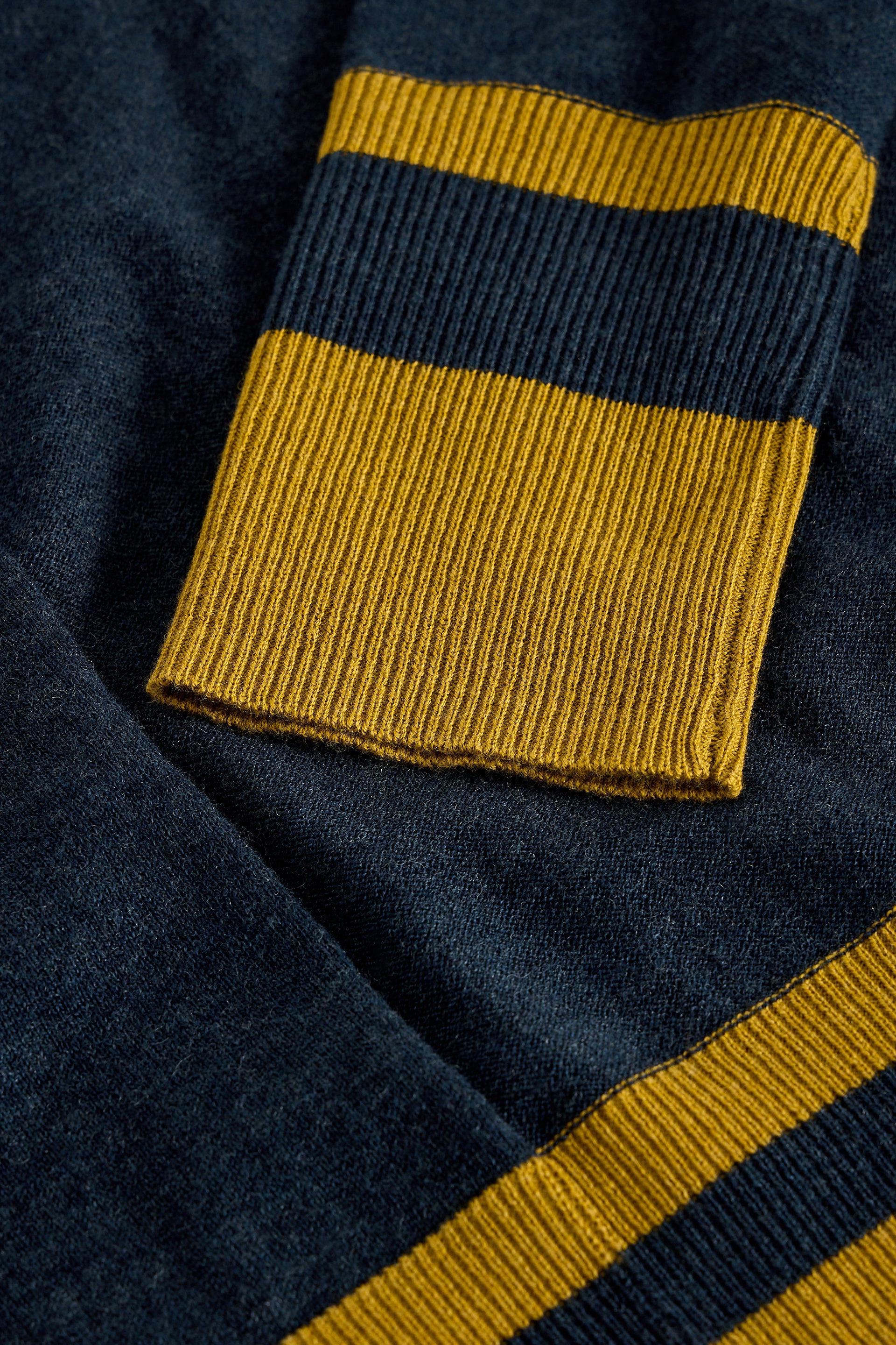Close-up of a ribbed knit garment in dark navy blue with bold mustard yellow horizontal stripes, showing the texture and construction of the sleeve cuff and hem.