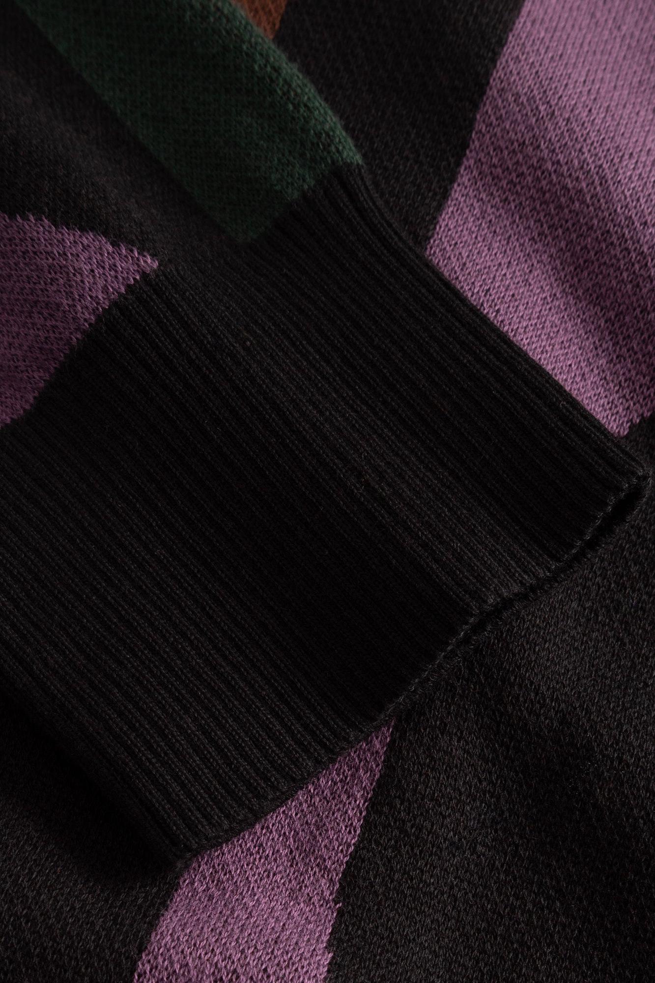 Close-up of a knit sweater showing a geometric color-block pattern with black, purple, and dark green sections.