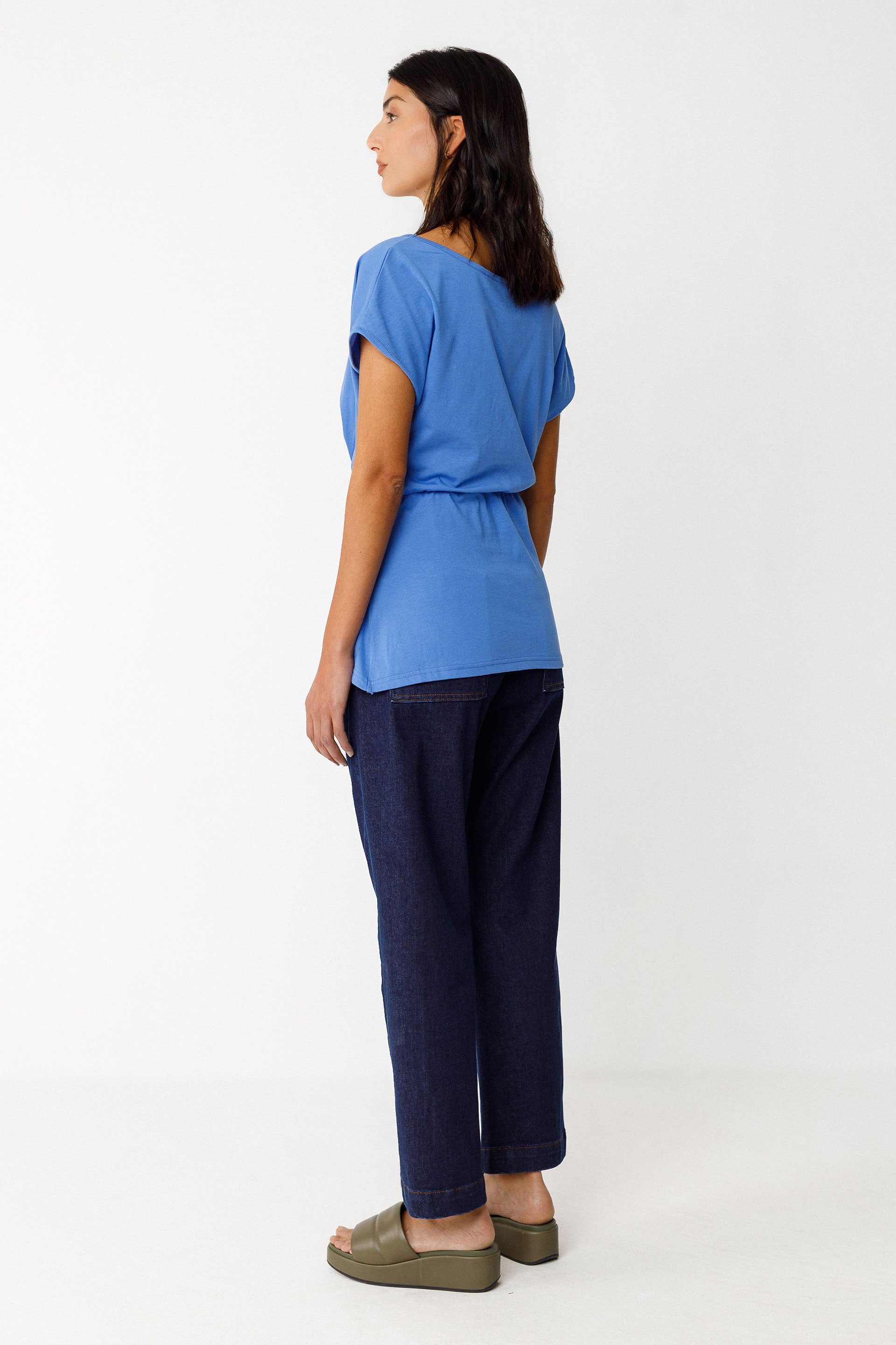 Woman wearing a blue top and dark pants on a white background