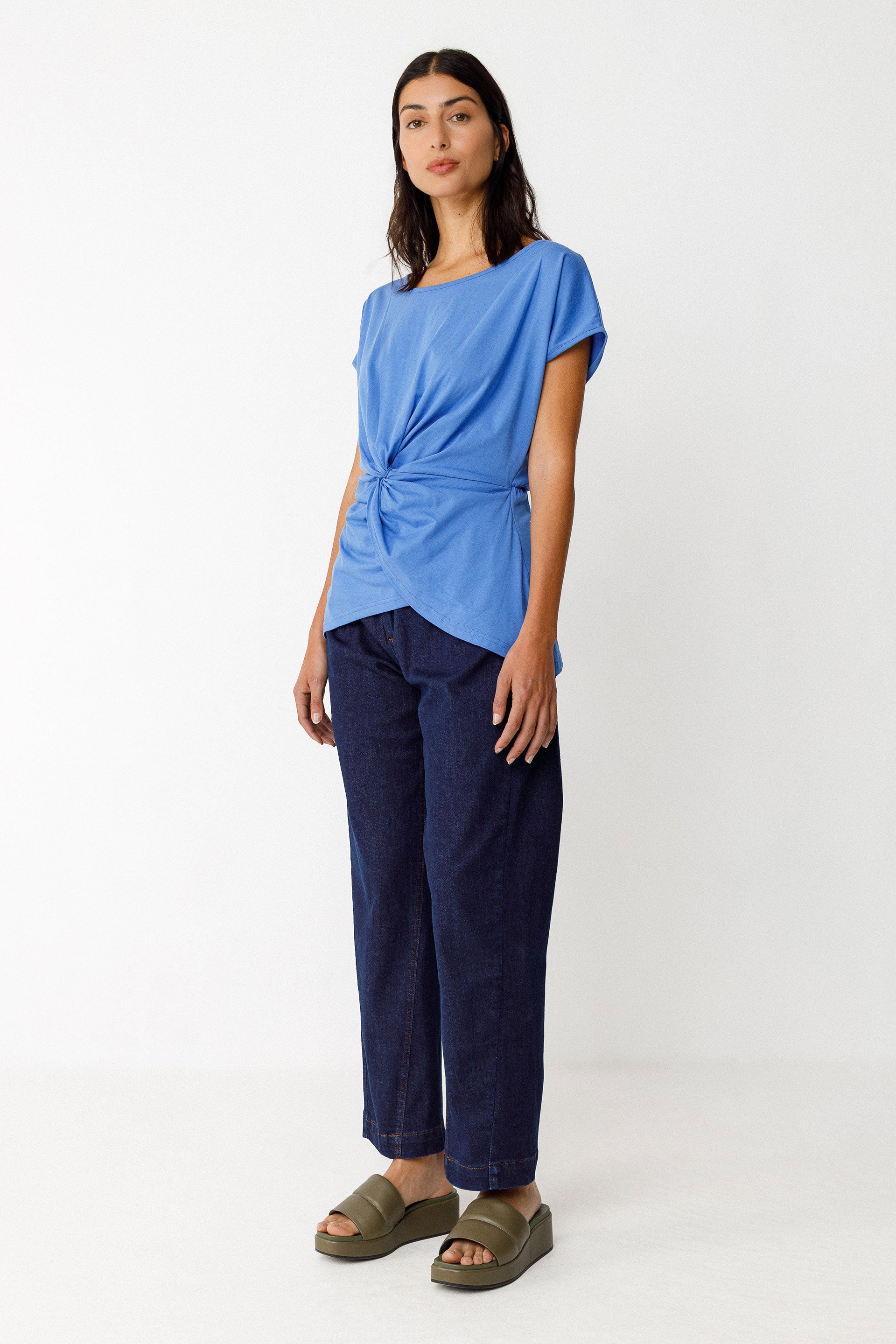Woman wearing a blue organic cotton knot top and navy pants on a white background