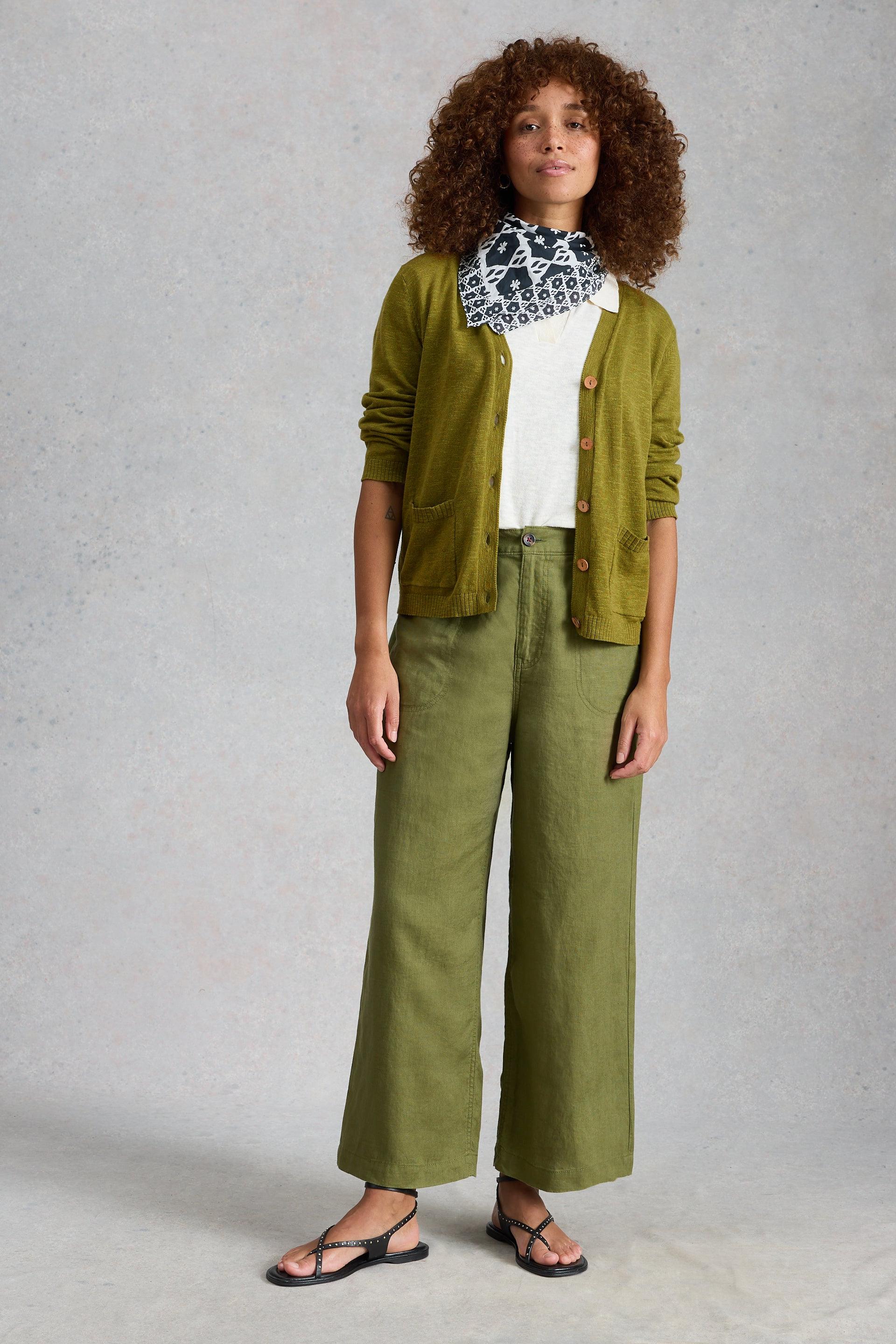 Woman wearing a green organic cotton cardigan, white shirt, and green pants against a gray background