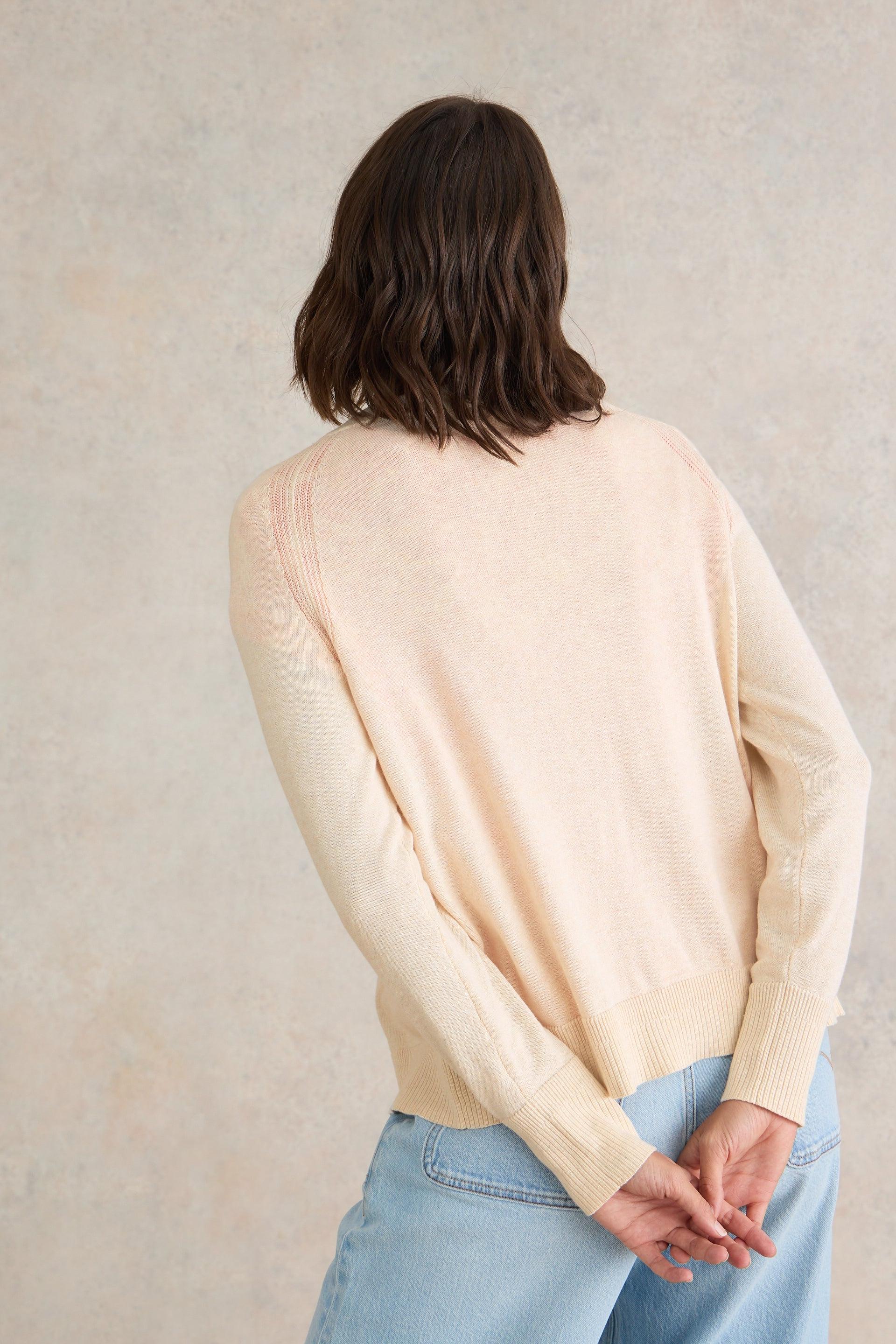 Person wearing a beige long sleeved cardigan and light blue jeans against a neutral background