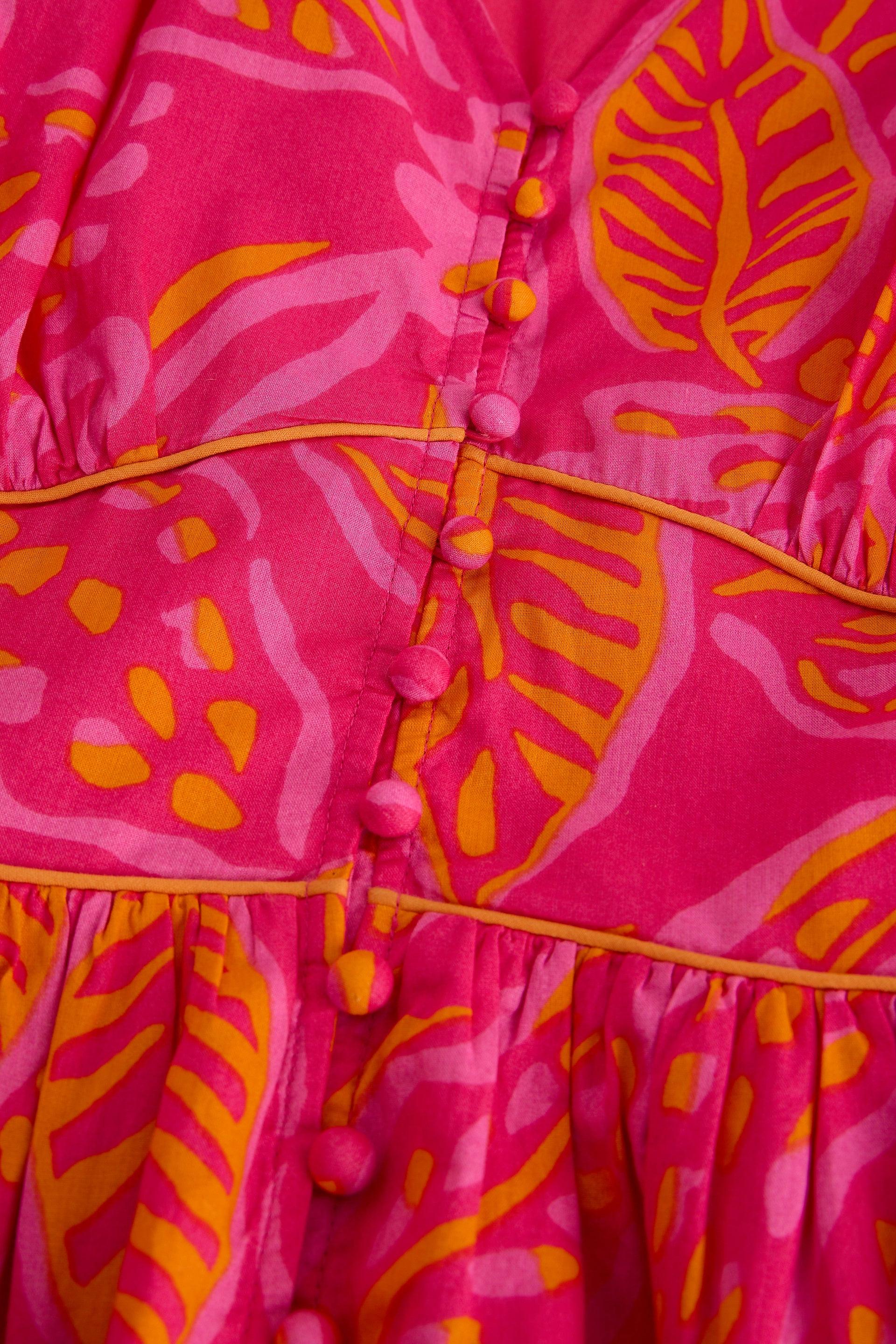 Close-up of a pink and orange organic cotton midi dress with leaf print and fabric-covered buttons.