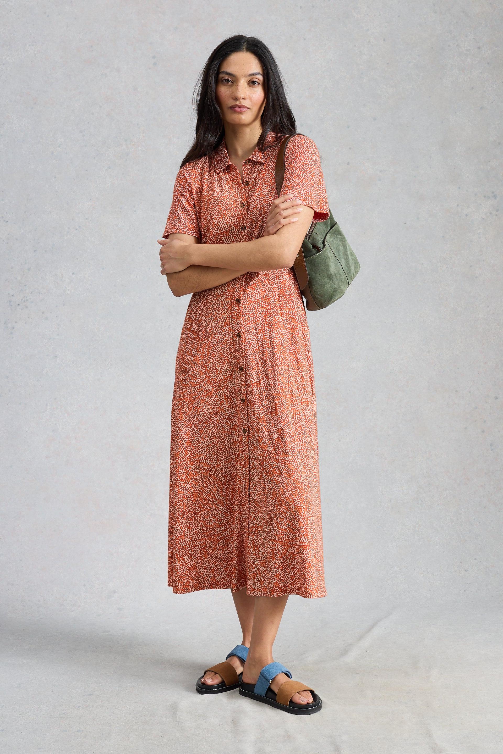 Woman wearing a red patterned midi dress with a green bag on a light gray background