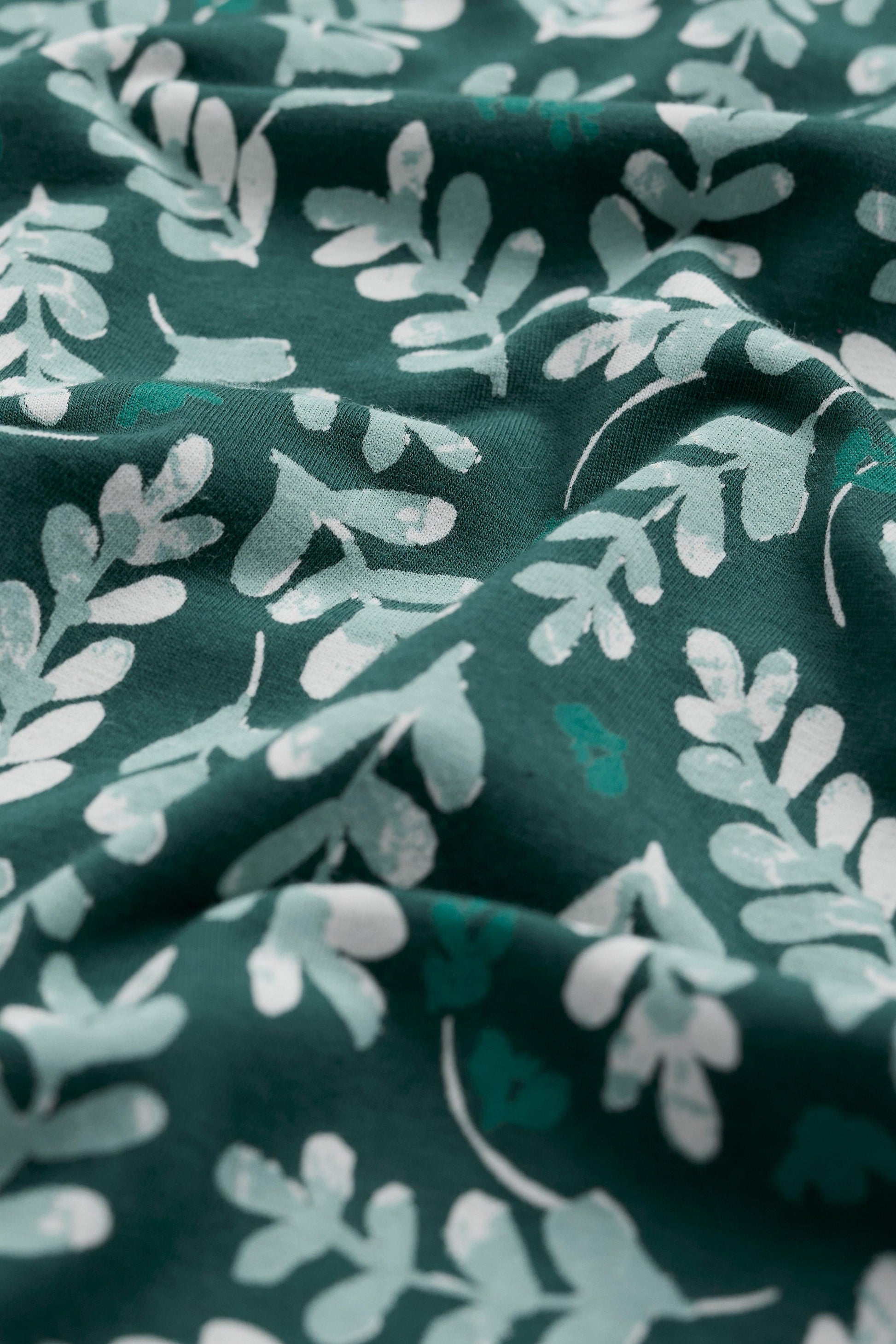 Organic cotton fabric with green and white leaf pattern on a dark green background