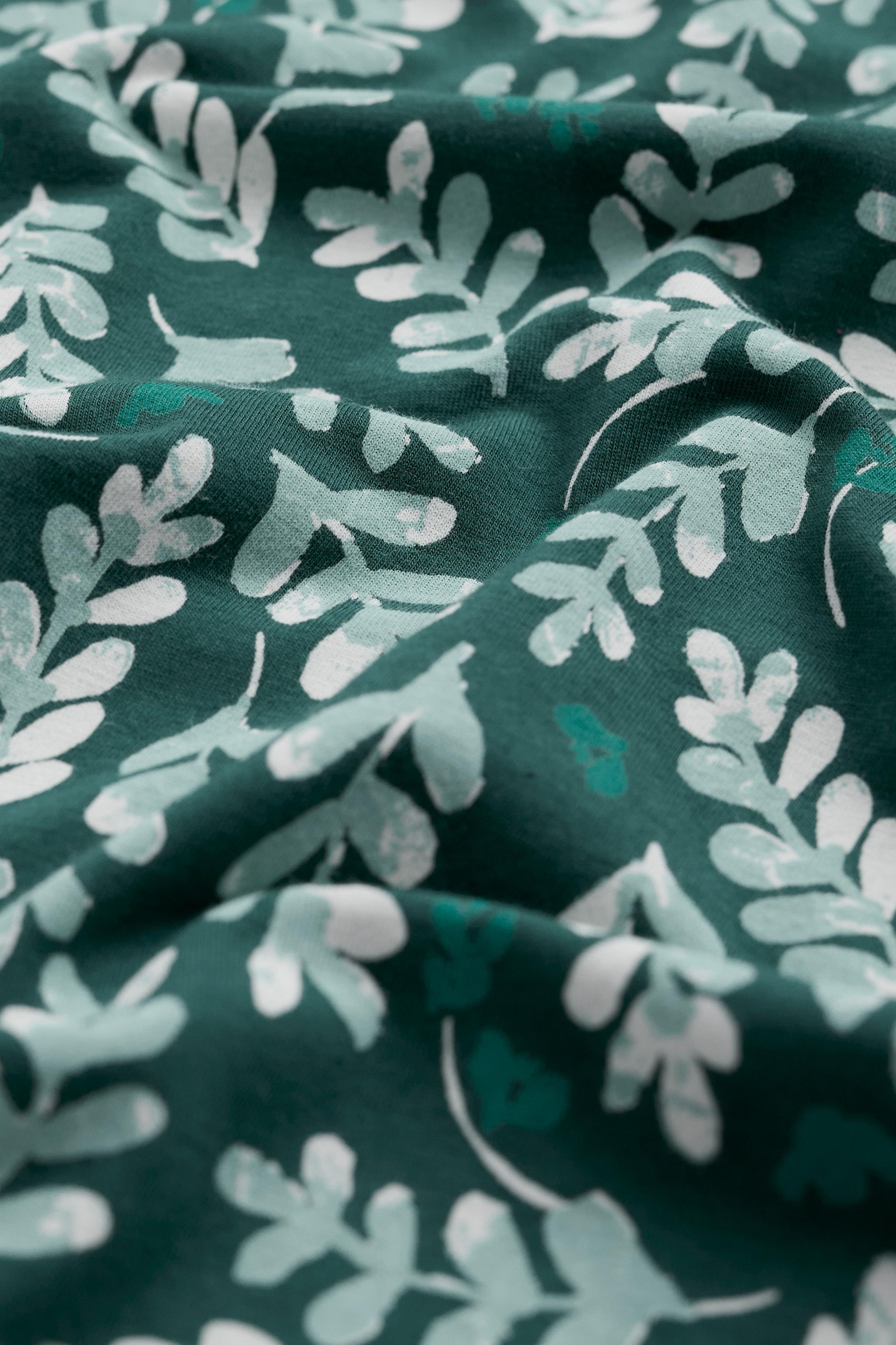 Organic cotton fabric with green and white leaf pattern on a dark green background
