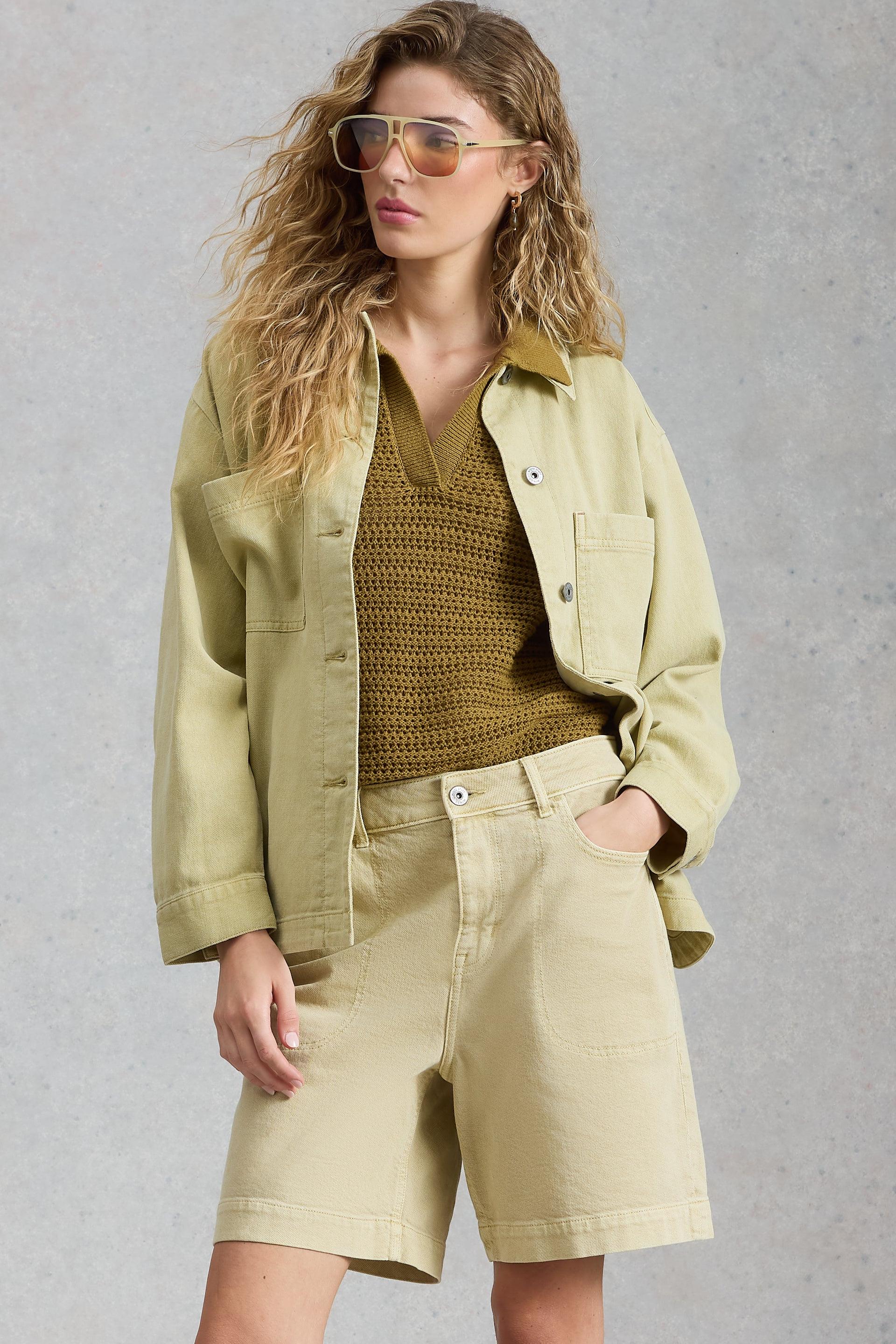 Woman wearing a green jacket and beige shorts against a gray background