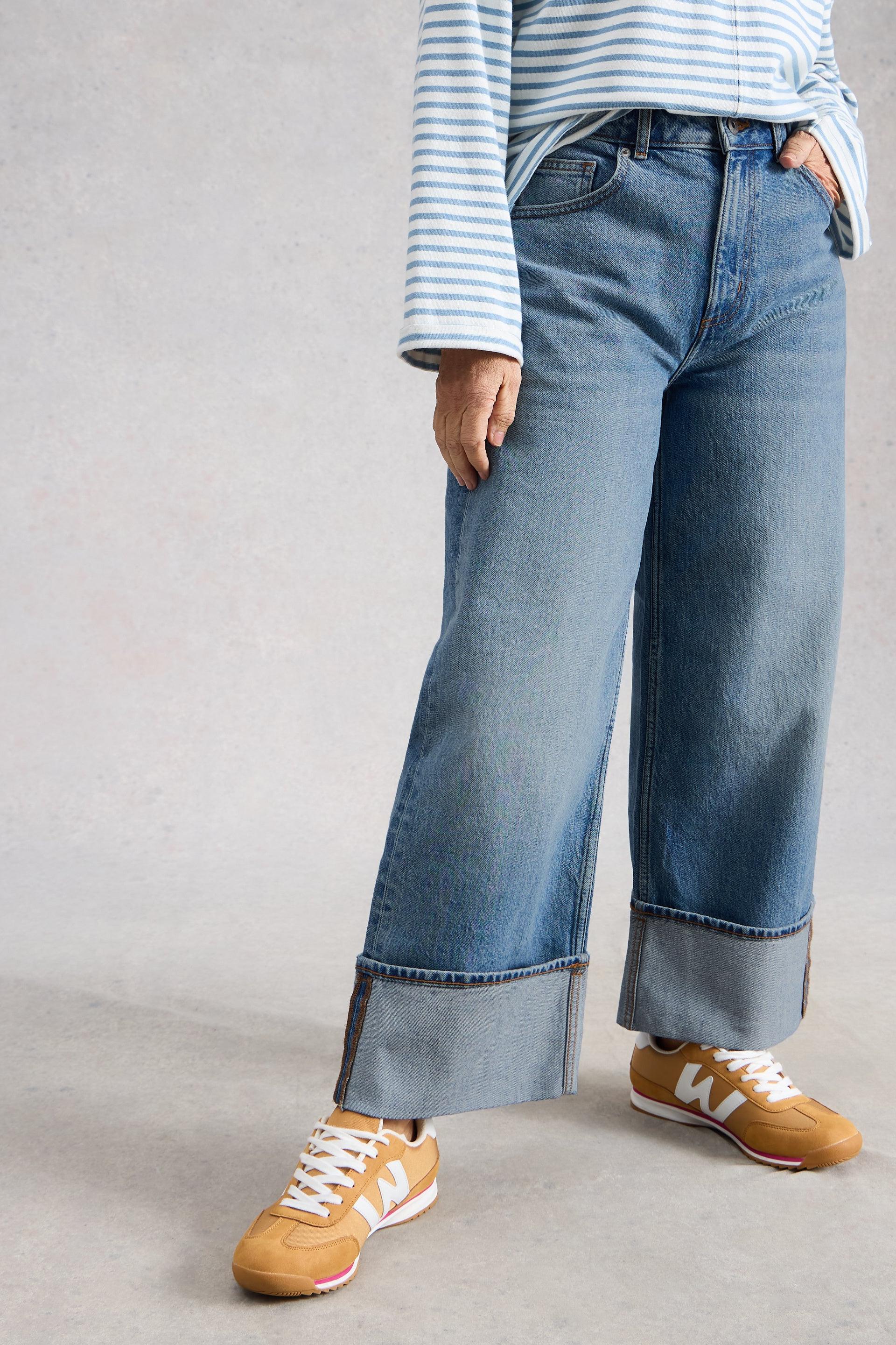Person wearing blue organic cotton straight jeans and brown shoes on a plain background