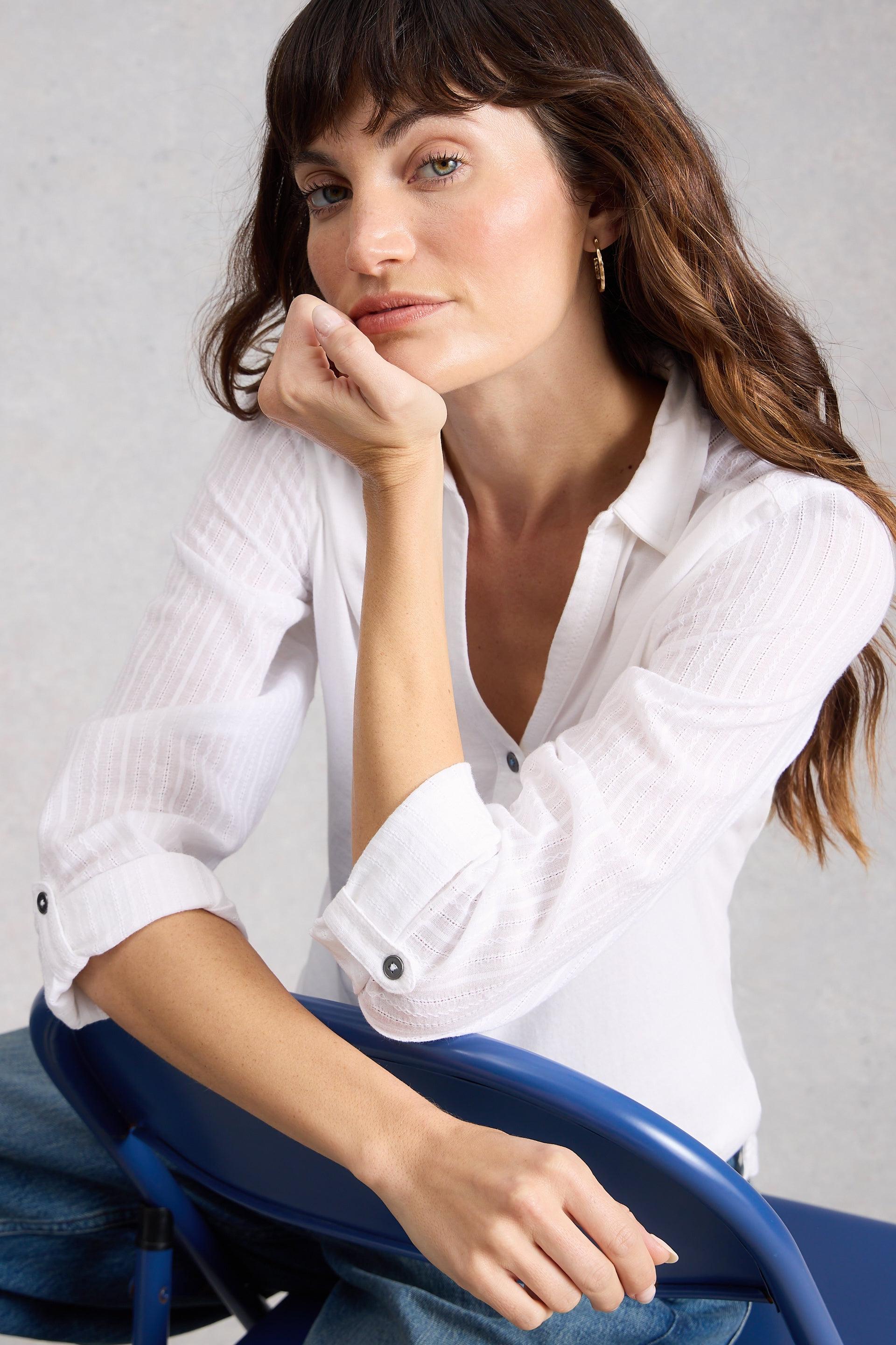 Woman in a white cotton shirt sitting on a blue chair against a gray background