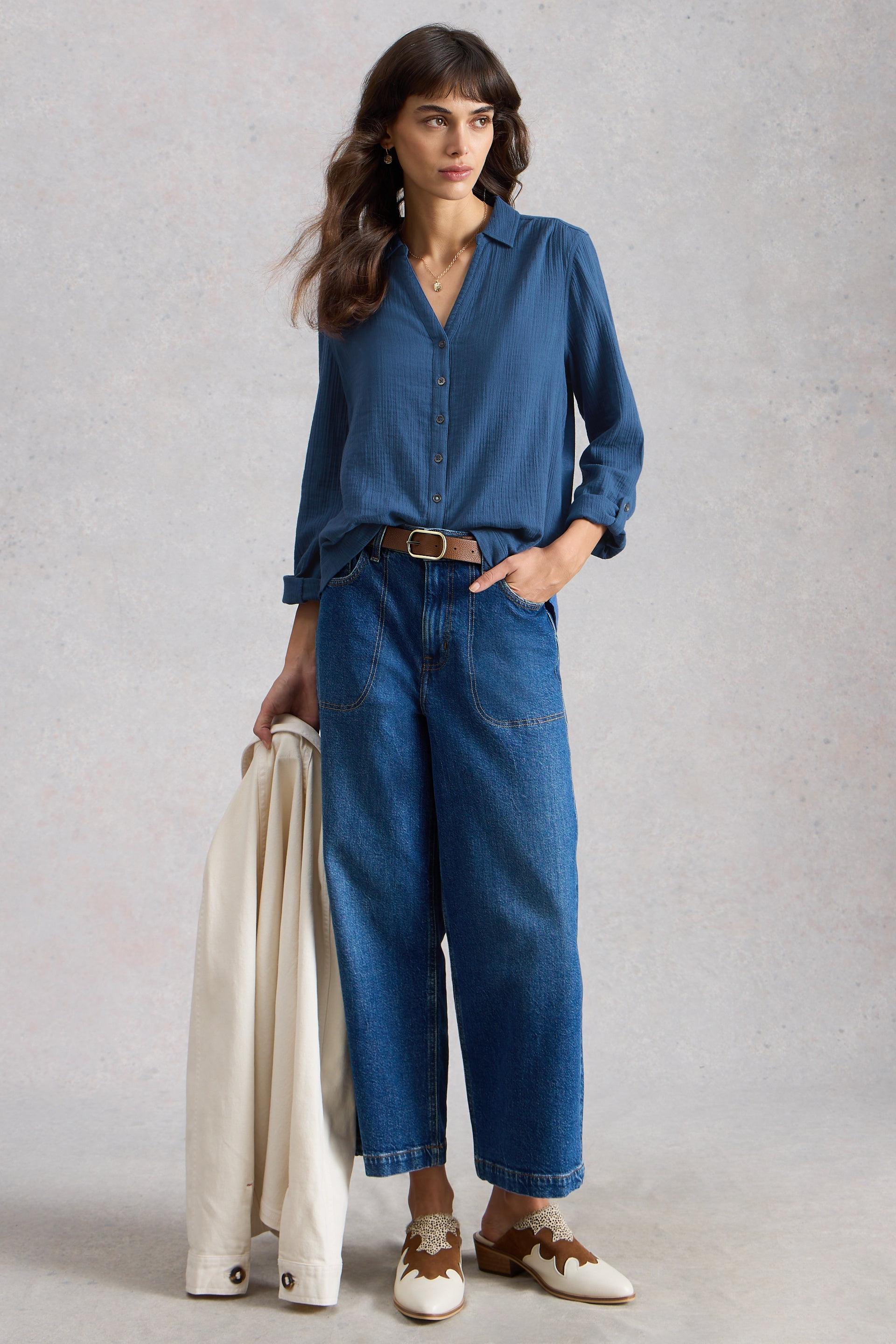 Woman wearing a blue denim outfit holding a beige jacket against a plain background