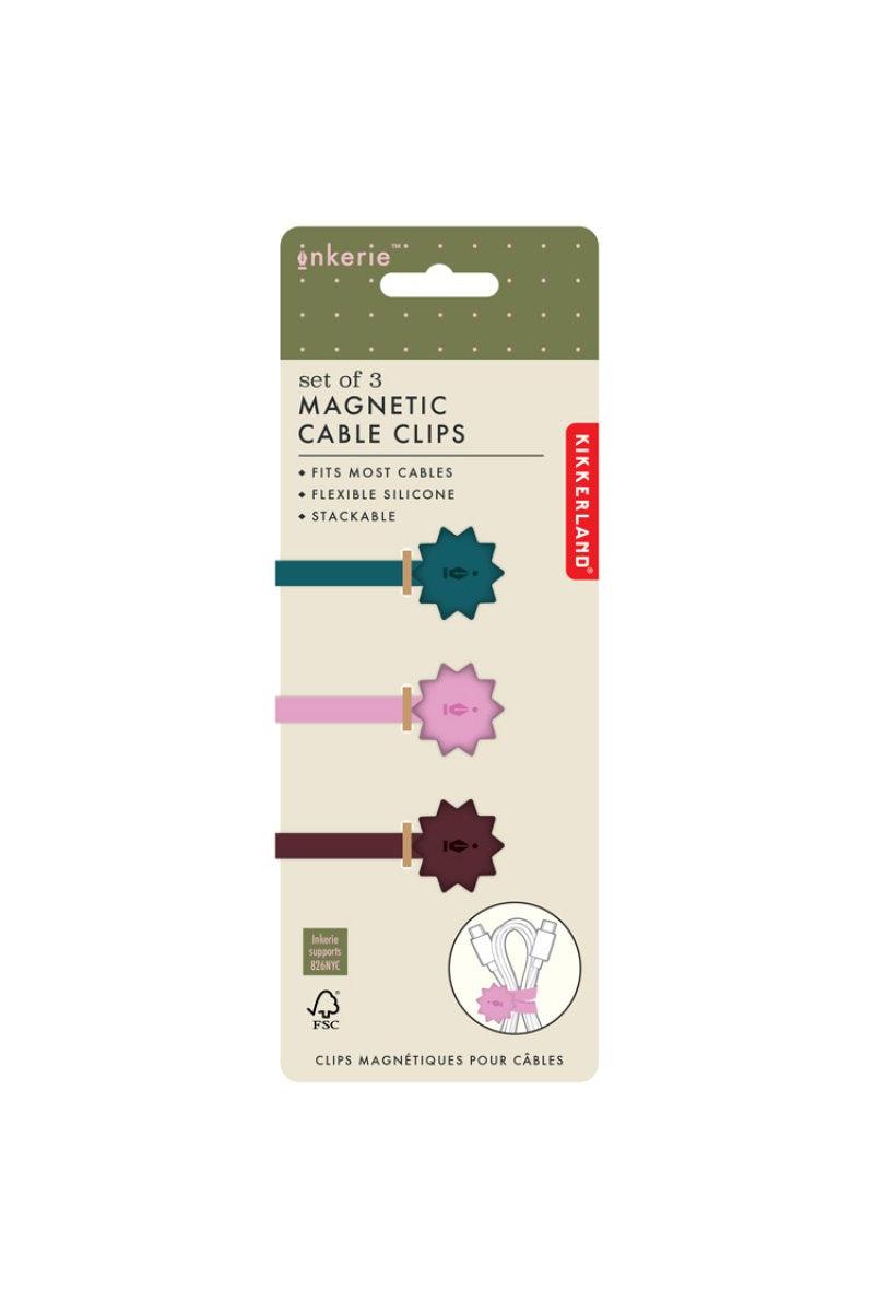 A retail package of enkerie Kikkerland magnetic cable clips, containing a set of three clips in teal, pink, and burgundy on a beige backing card with a green header.