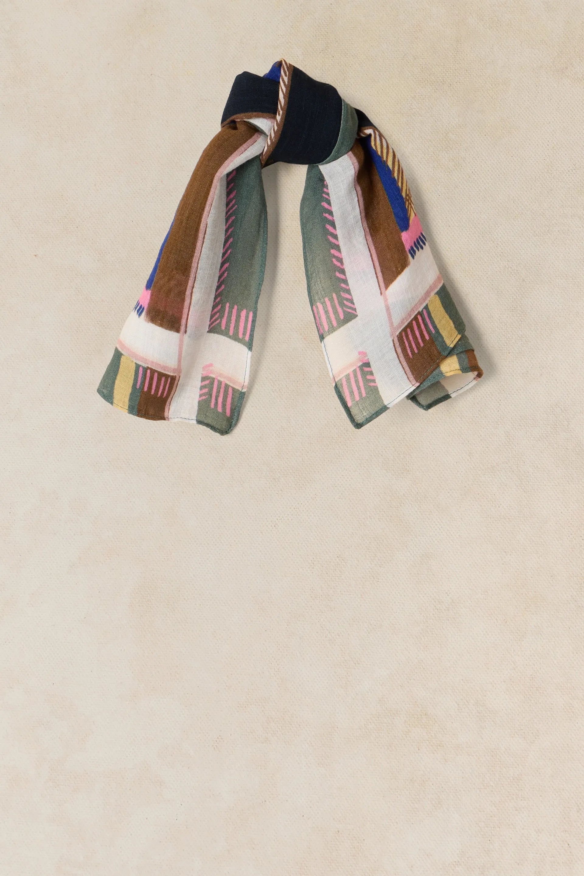 A patterned knotted scarf featuring brown, green, and pink abstract designs on a light beige background