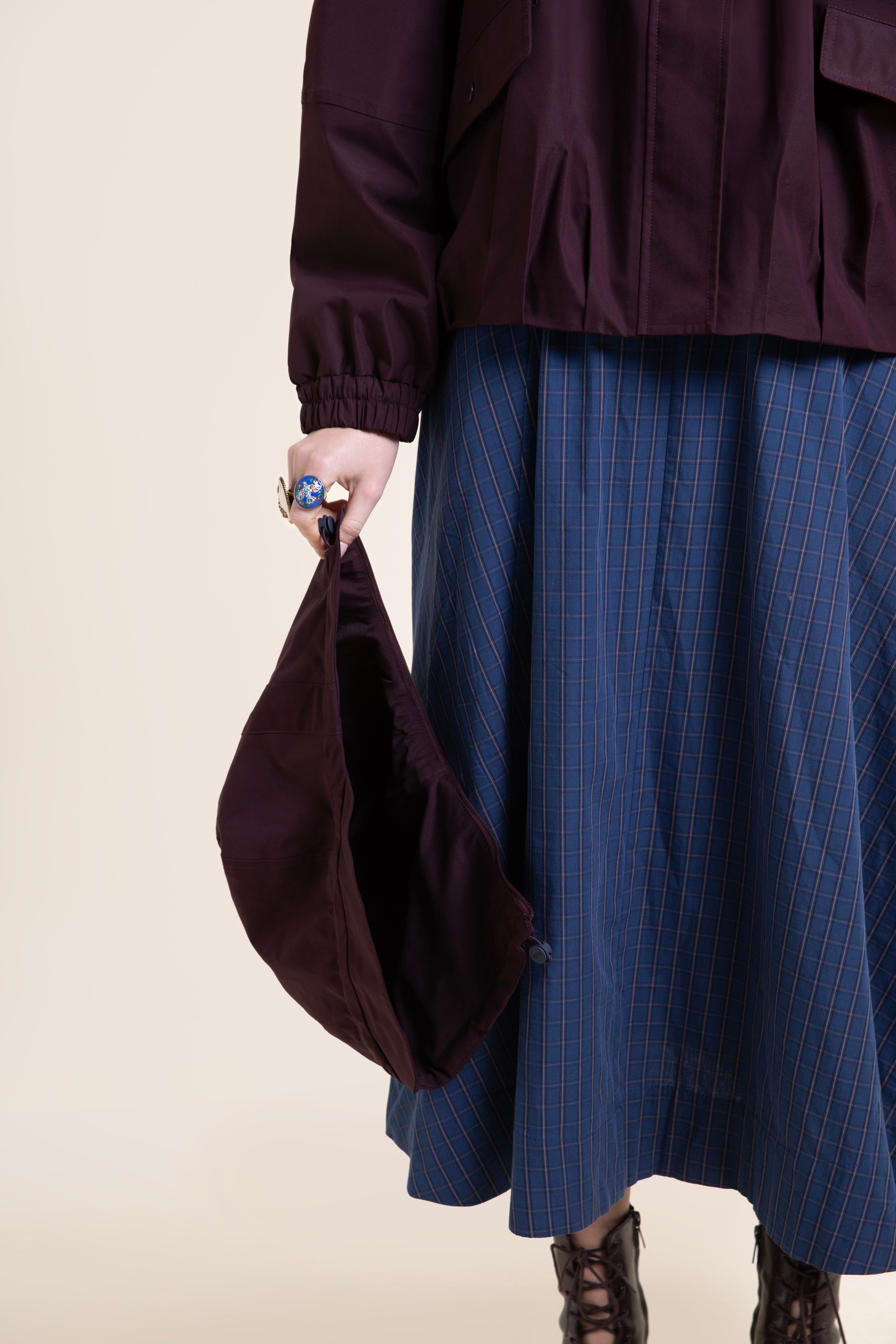 Person wearing a dark burgundy waterproof coat and blue plaid skirt, holding a matching recycled polyester bucket hat.