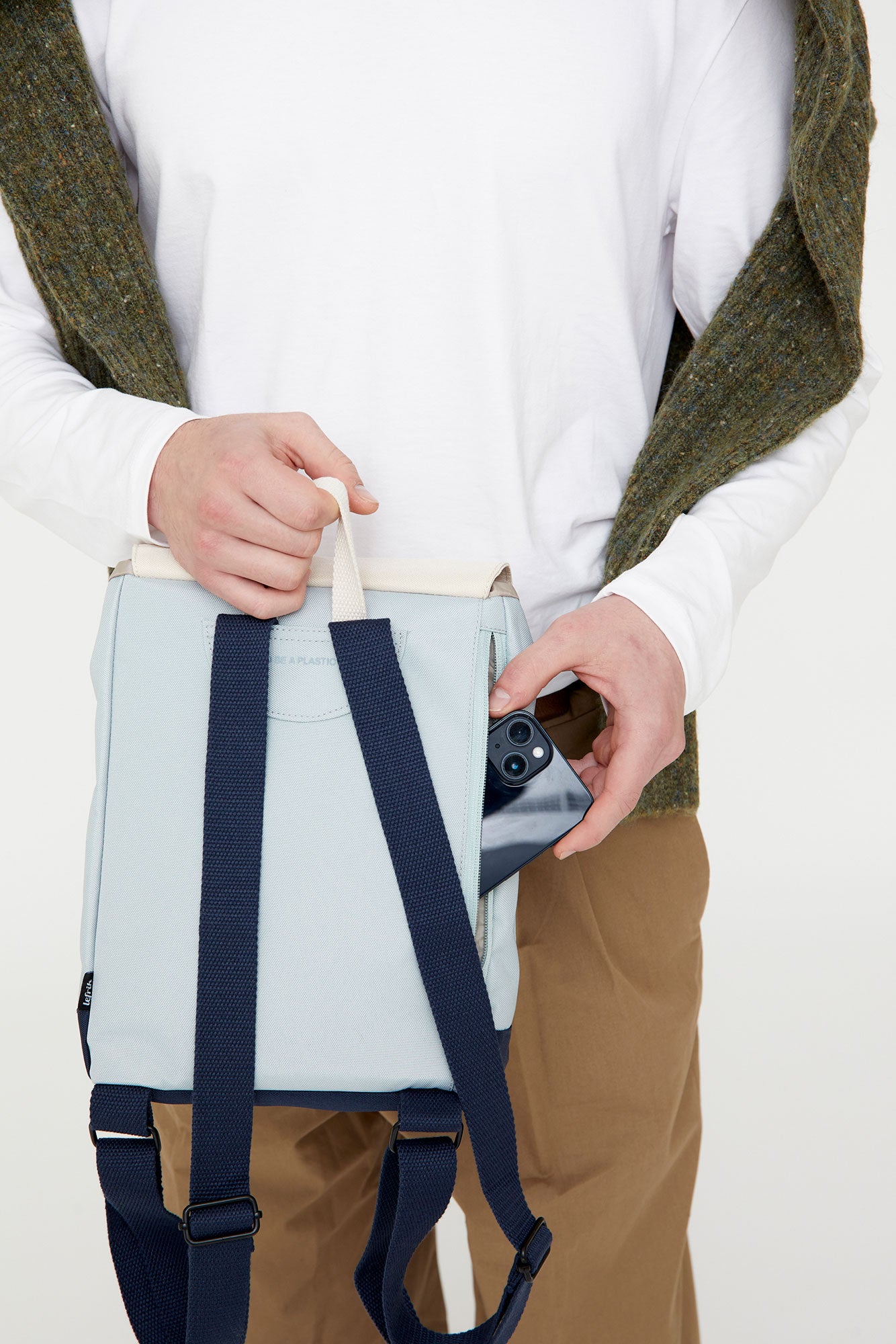 Person holding a light blue backpack with dark blue straps against a white background