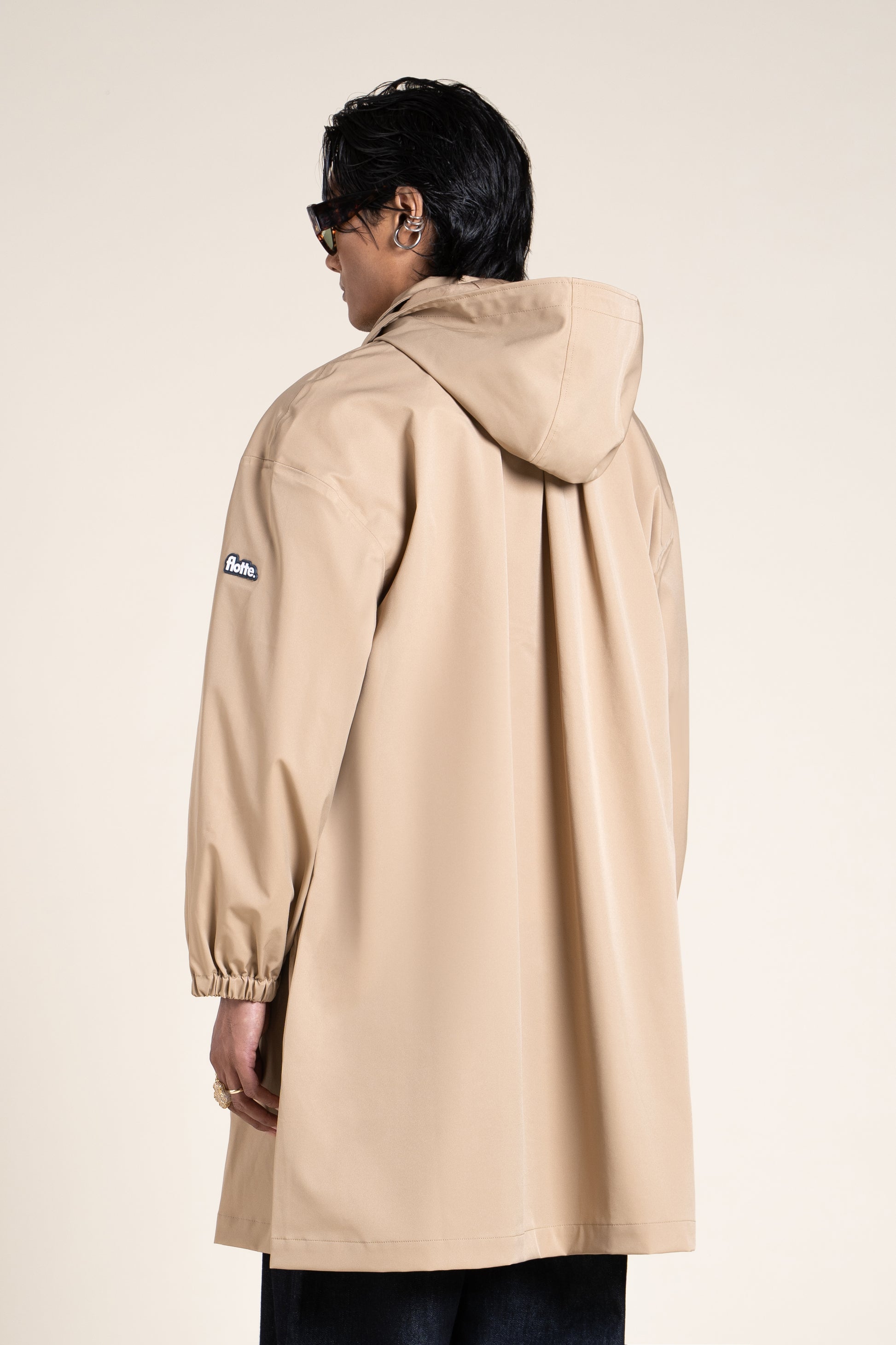 Back view of a person wearing a beige Flotte waterproof coat and a brown woven bucket hat.