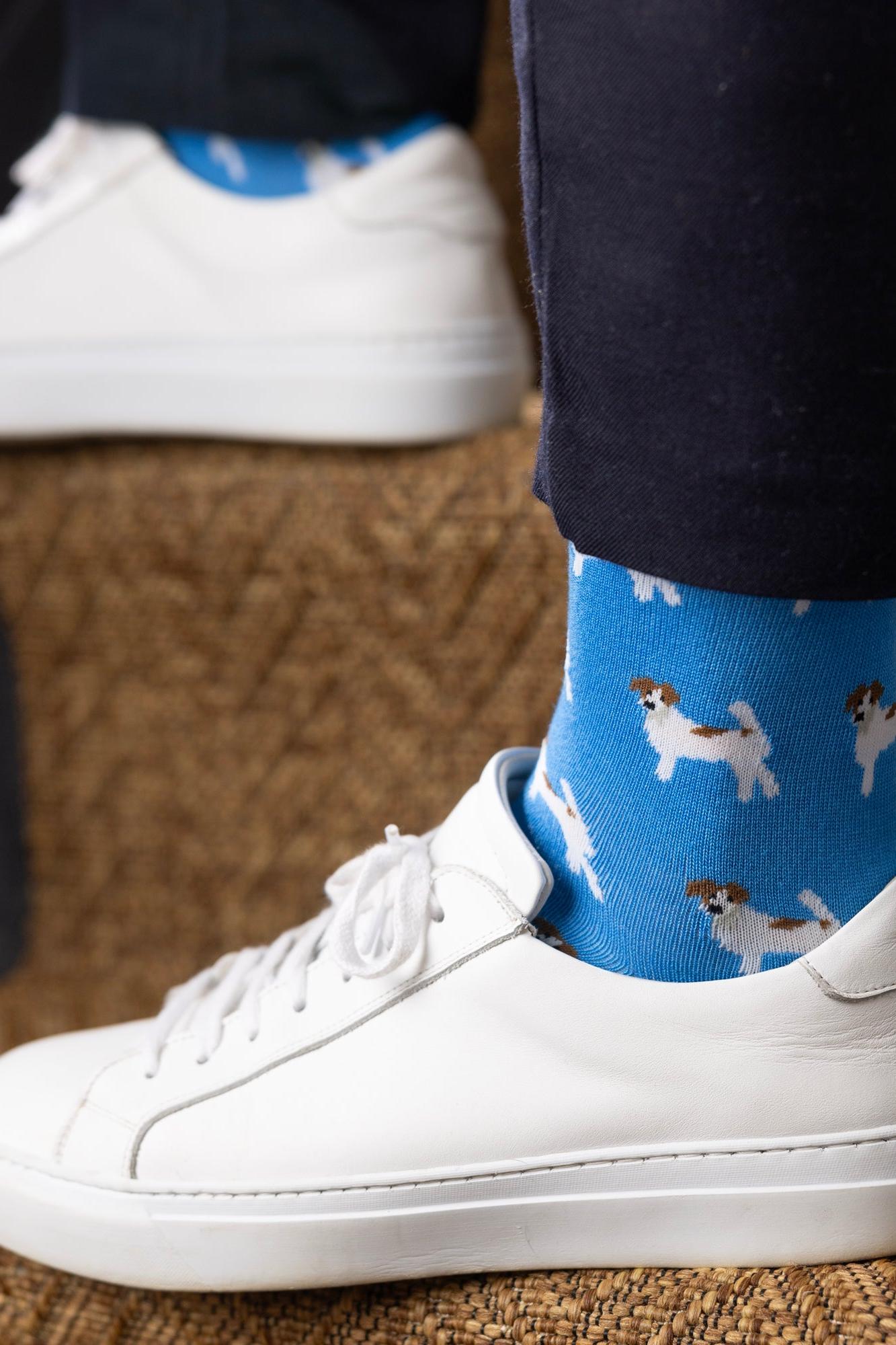 Close-up of a person wearing blue bamboo socks with terrier dog patterns and white leather sneakers on carpeted stairs.