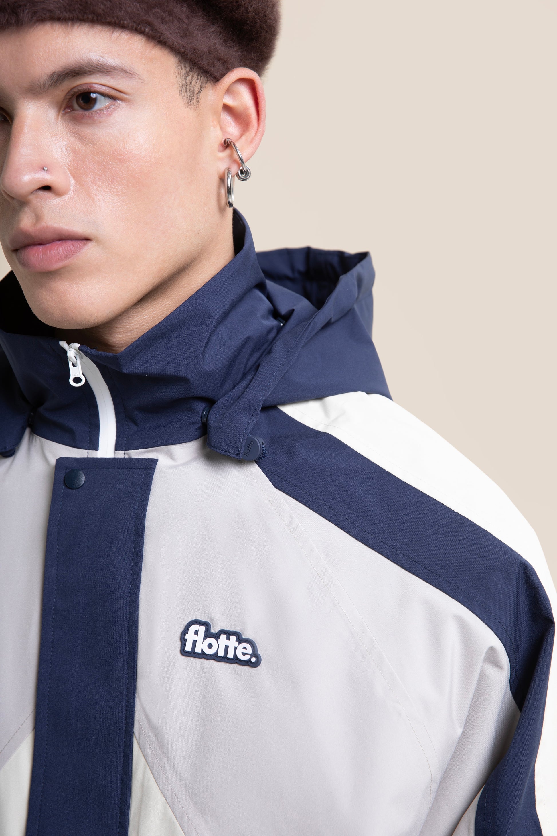 Close up of a person wearing a navy and beige unisex waterproof jacket with a logo patch.