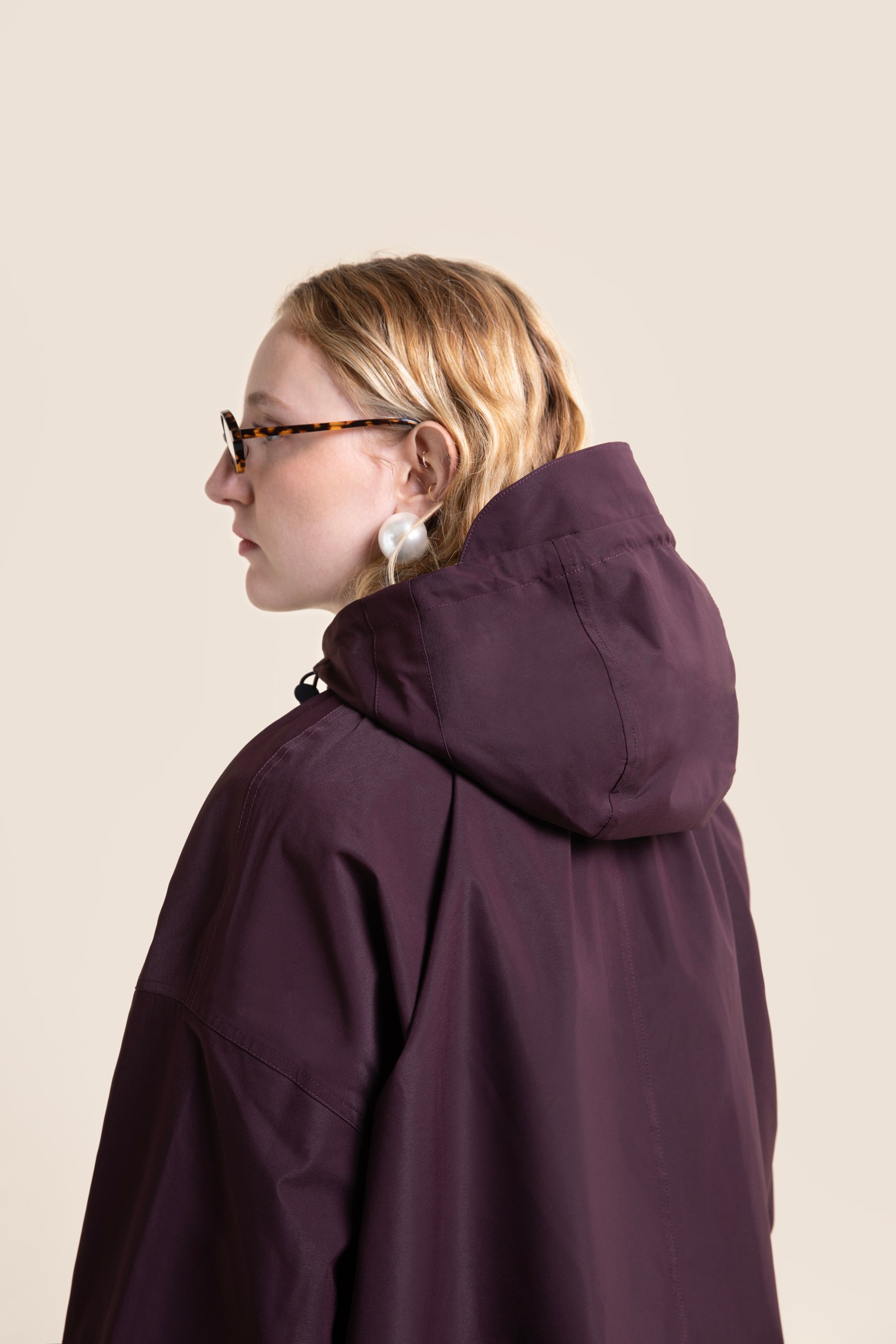 Profile view of a person wearing a stylish, deep purple waterproof Flotte coat with a hood.