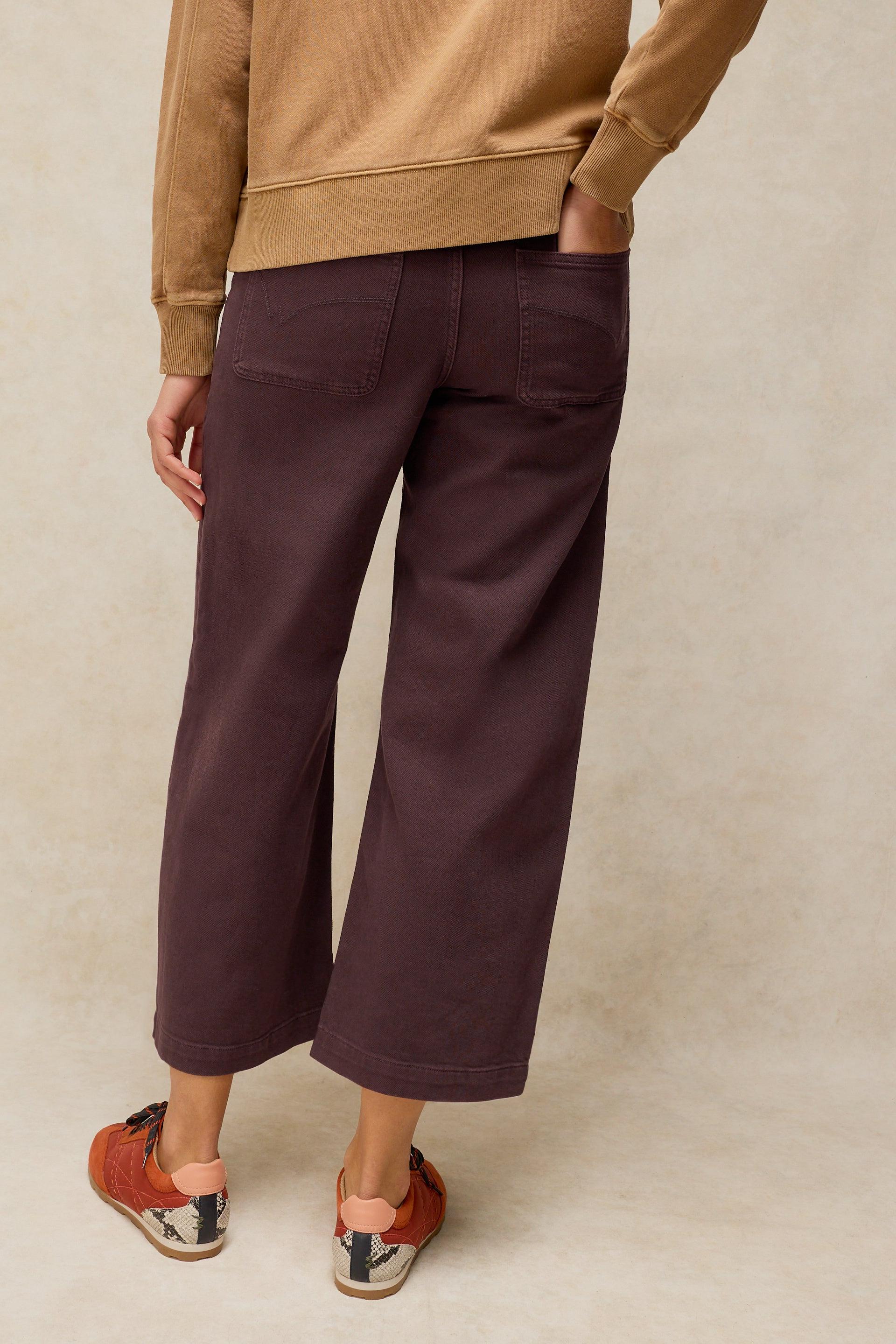 A person viewed from behind wearing wide-leg dark brown organic cotton trousers and patterned sneakers