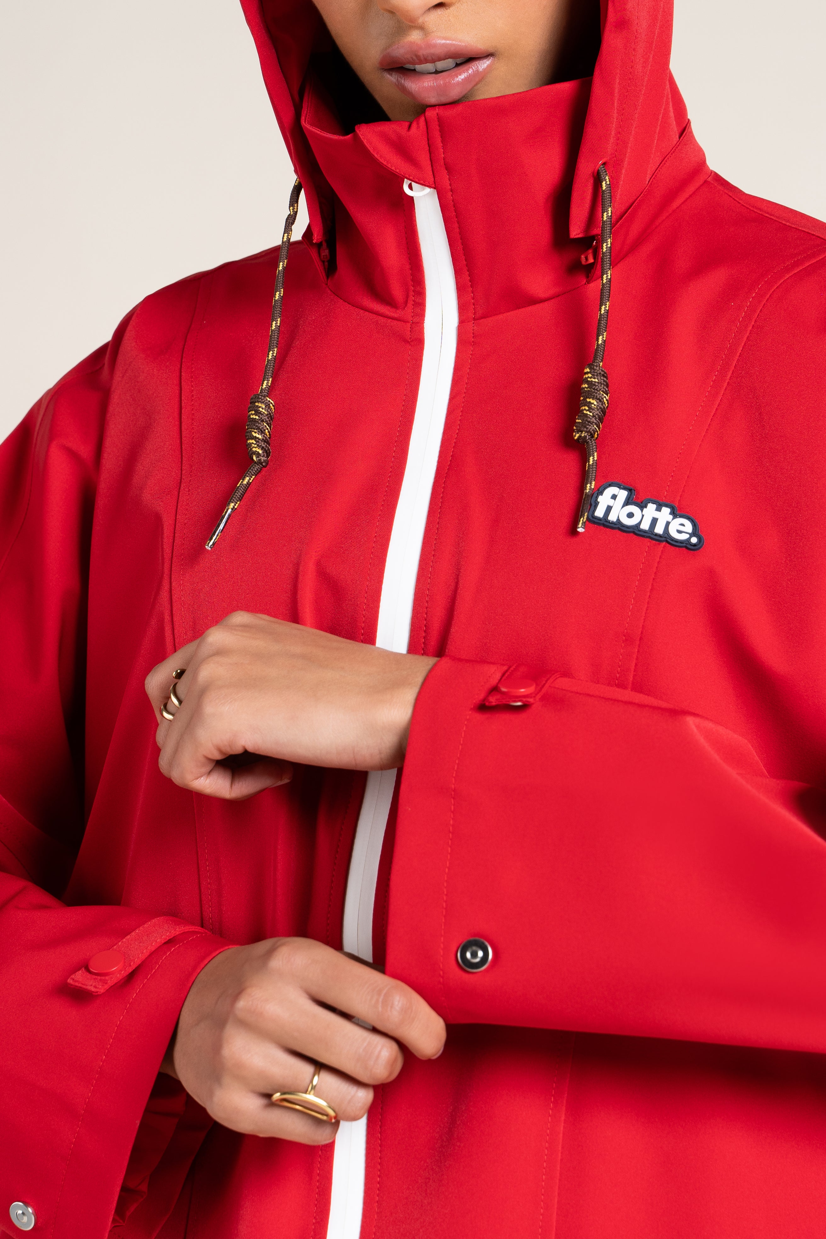 Person wearing a bright red waterproof Flotte raincoat with a white zipper and hood.