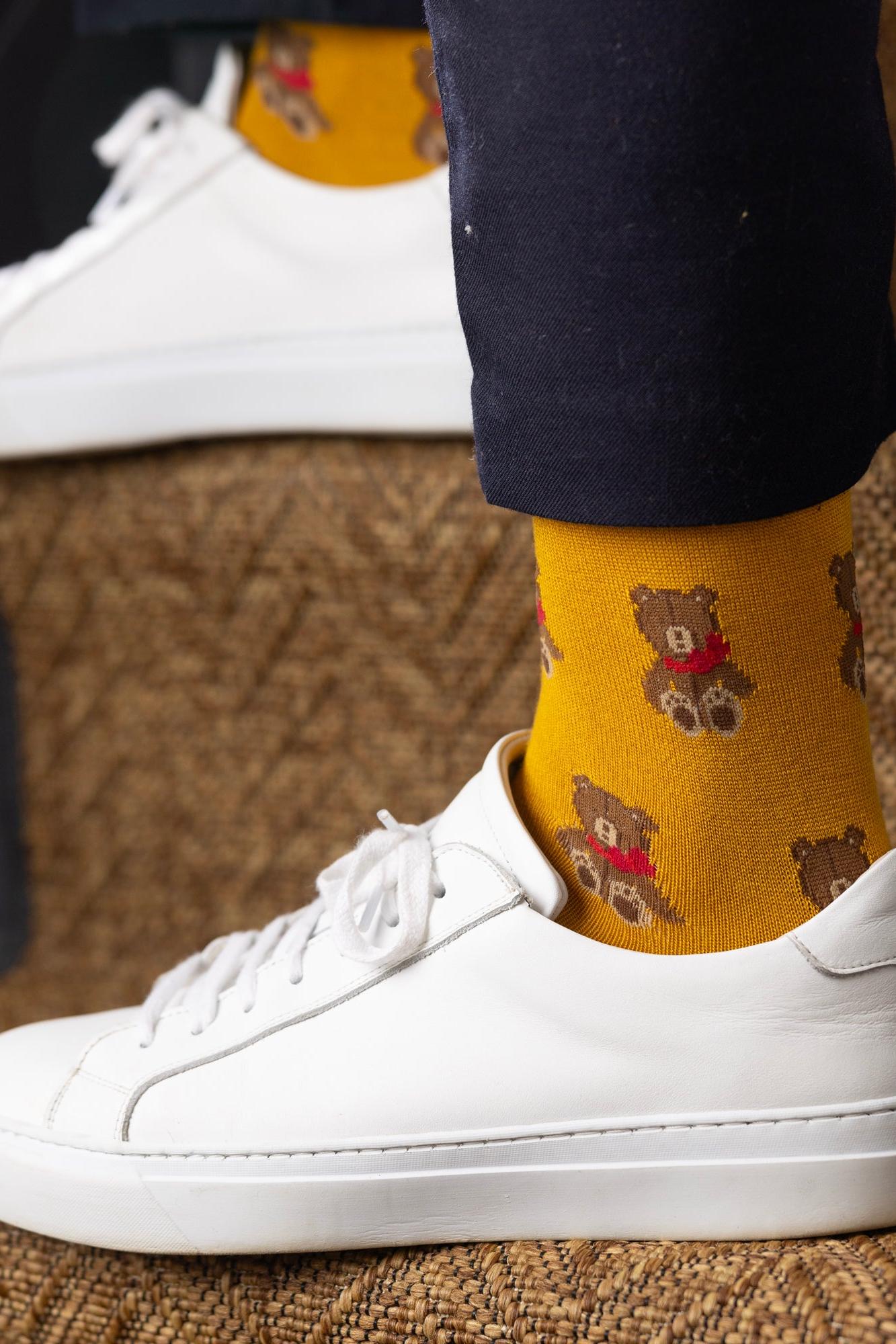 Close-up of a person wearing mustard yellow teddy bear print fun socks with white sneakers on a carpeted staircase.