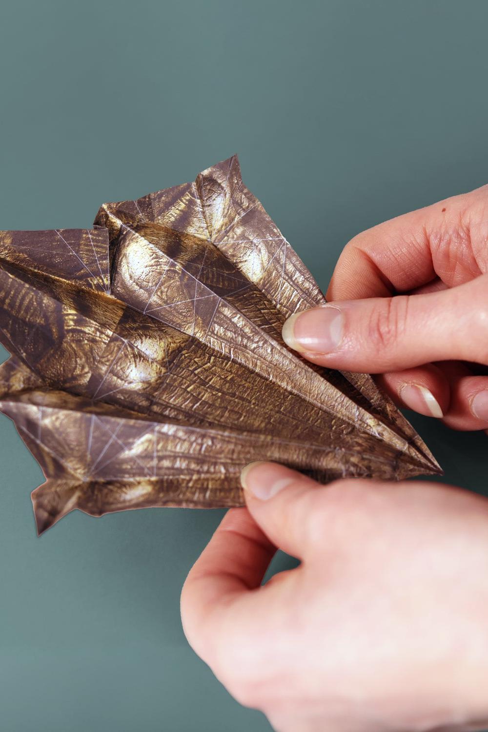 Hands holding a metallic leaf-like object against a green background